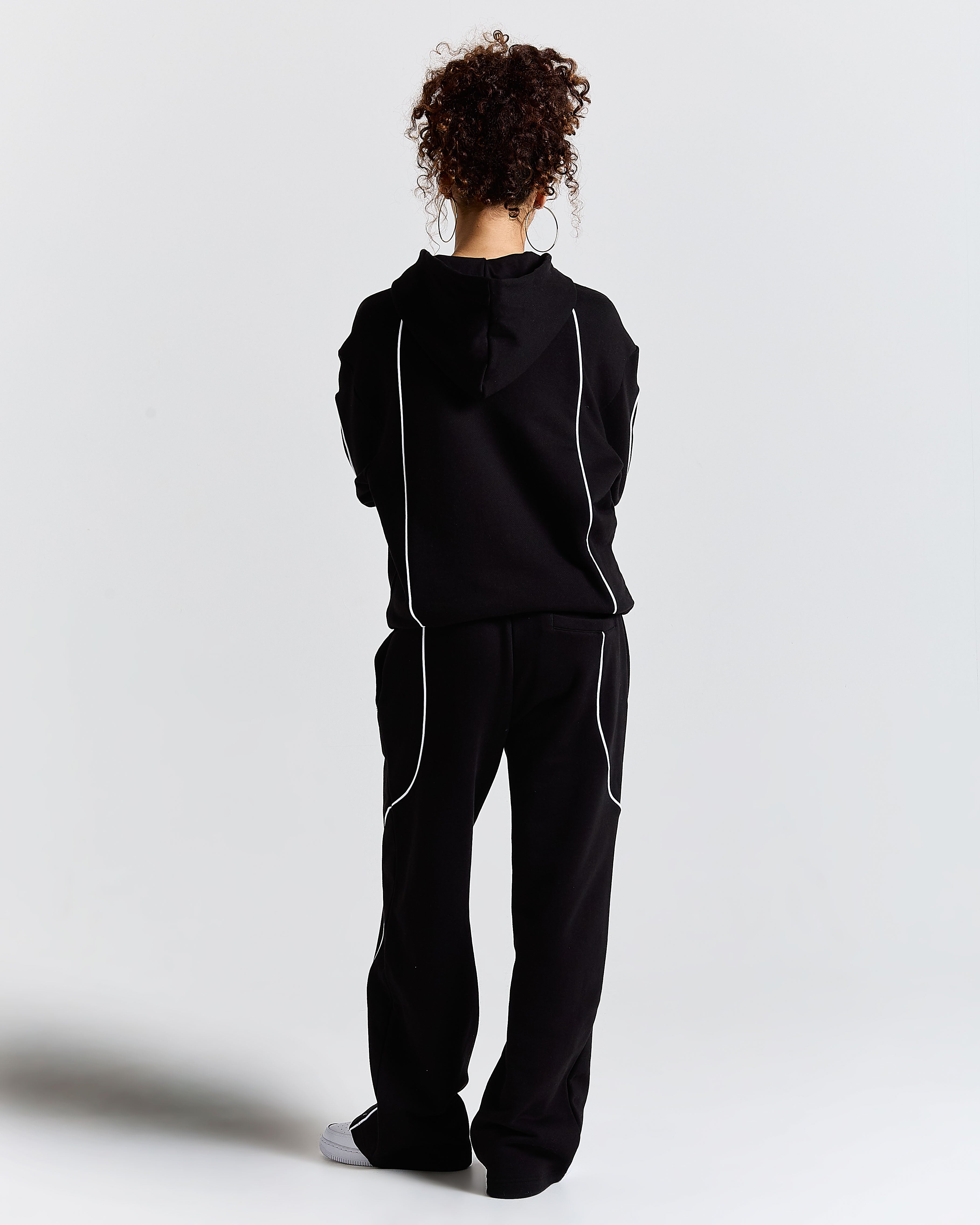 Person wearing a black tracksuit with white stripes on a light grey background