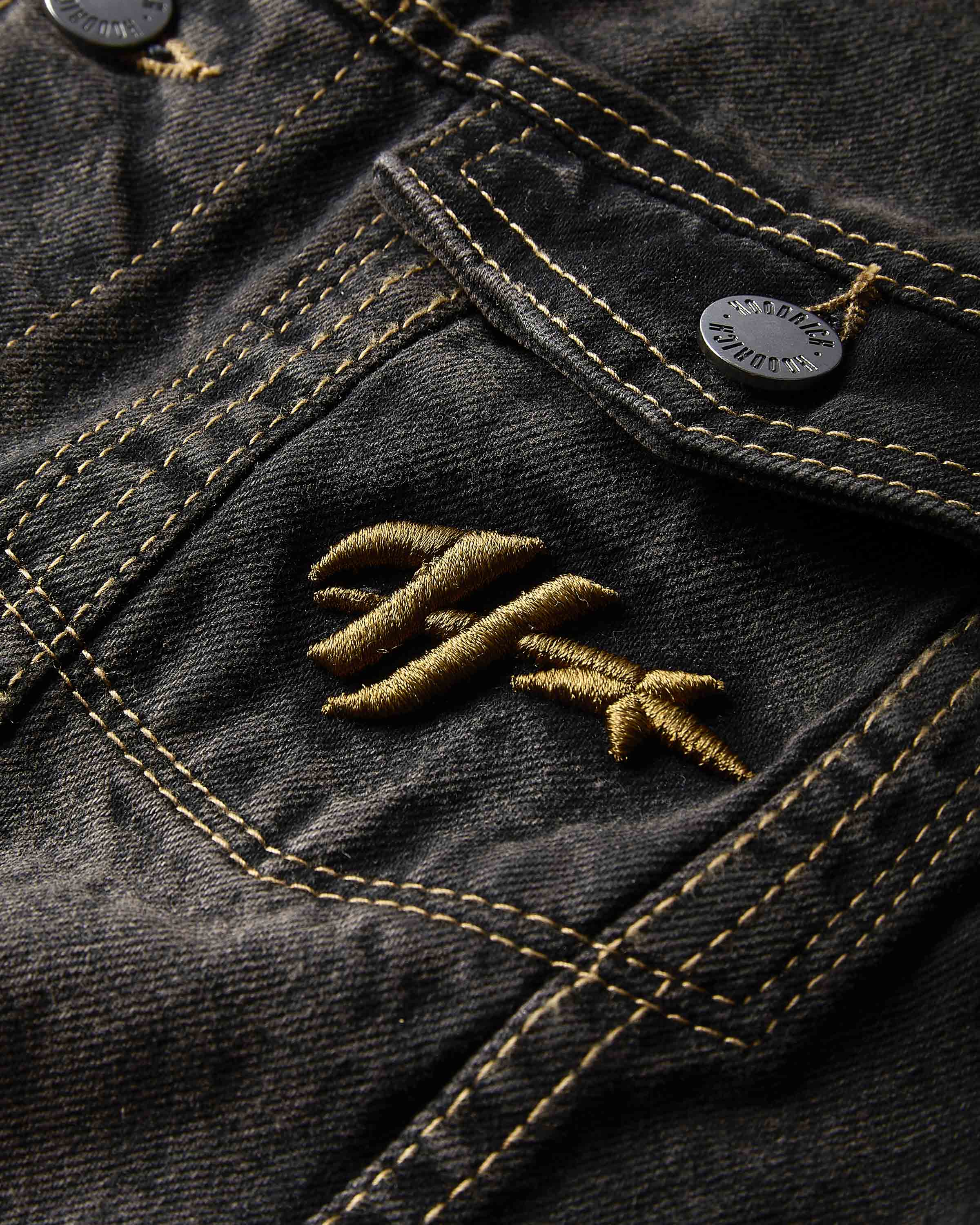 Close-up of a dark denim jacket with an embroidered logo on the pocket.