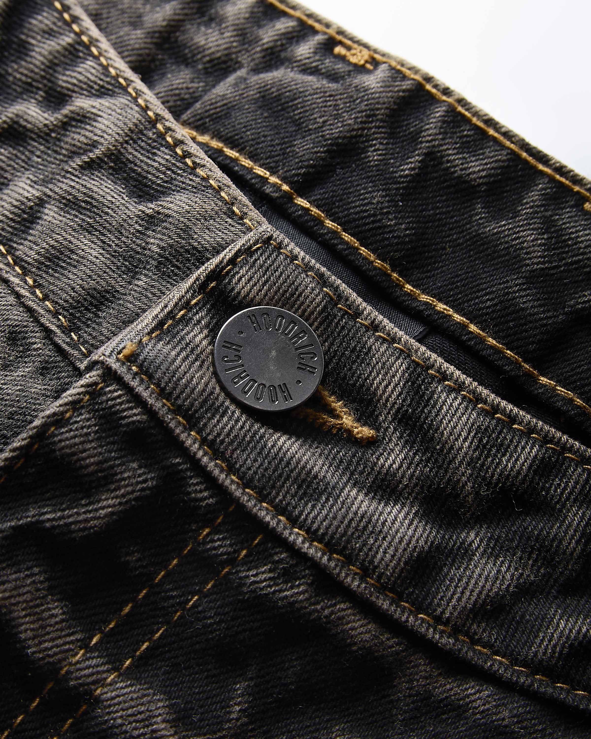 Close-up of dark gray washed denim jeans showing the button closure, contrast gold stitching, and detailed denim texture.
