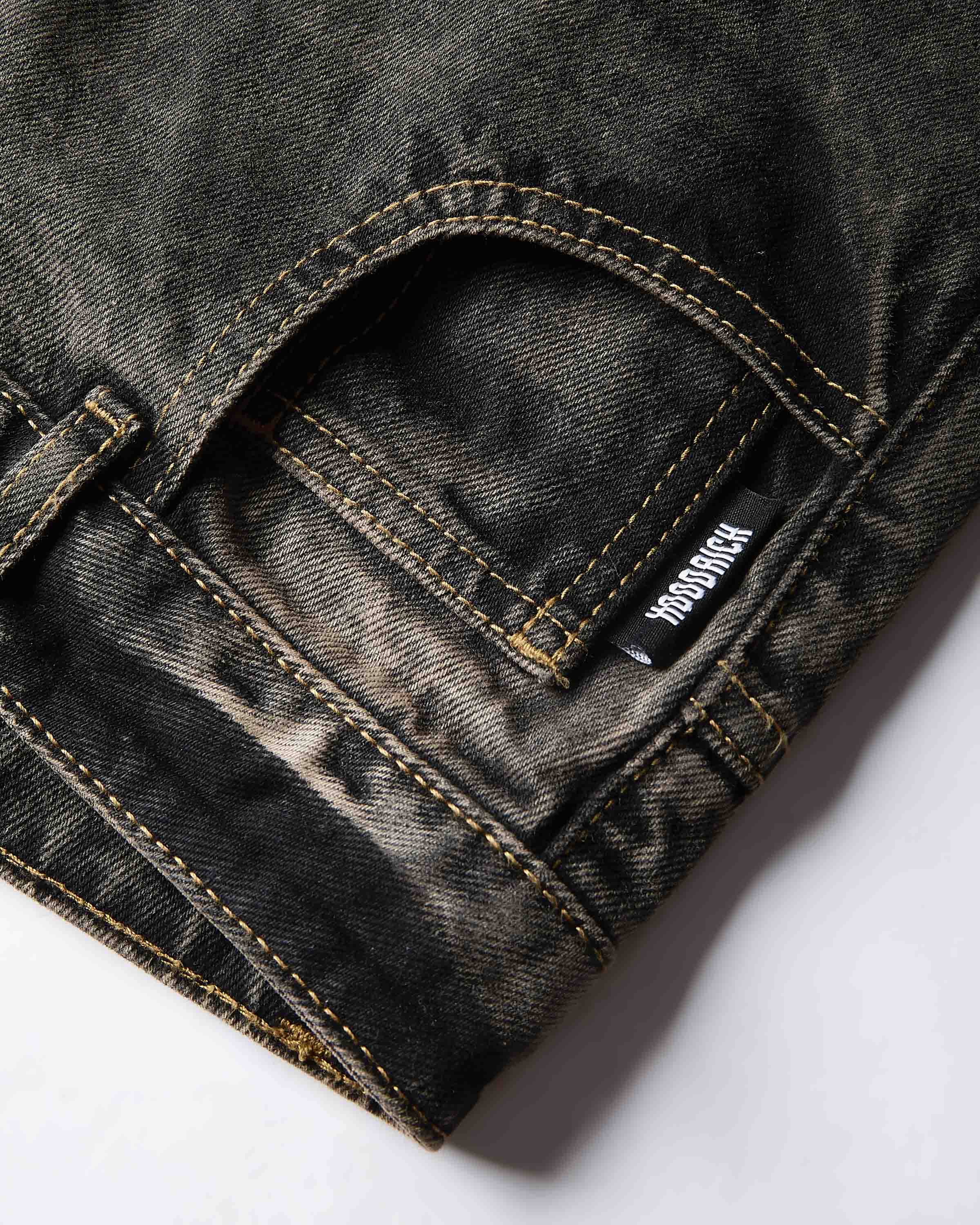 Close-up of a dark washed denim pair of jeans showing the back pocket with HOODRICH contrast stitching and a visible brand tag.