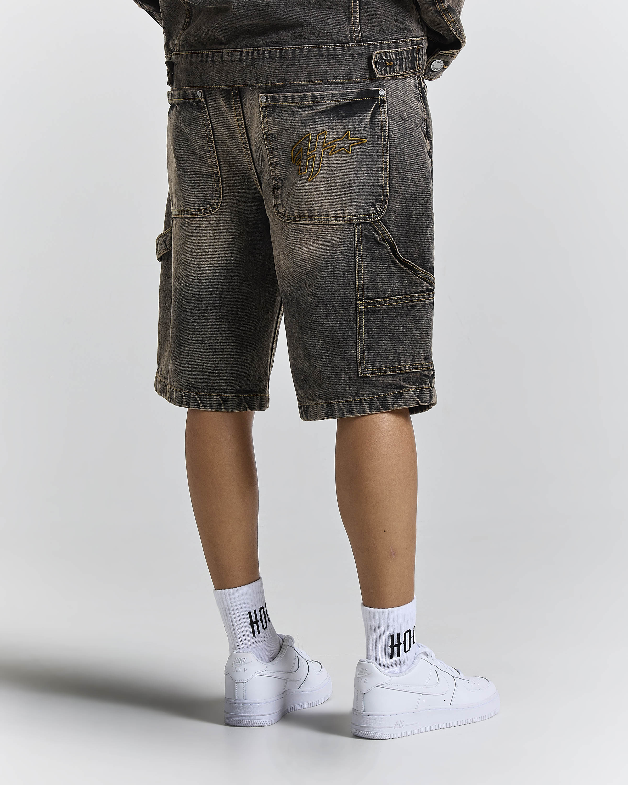 Person wearing dark denim shorts and white sneakers with 'HOODRICH' socks on a light gray background