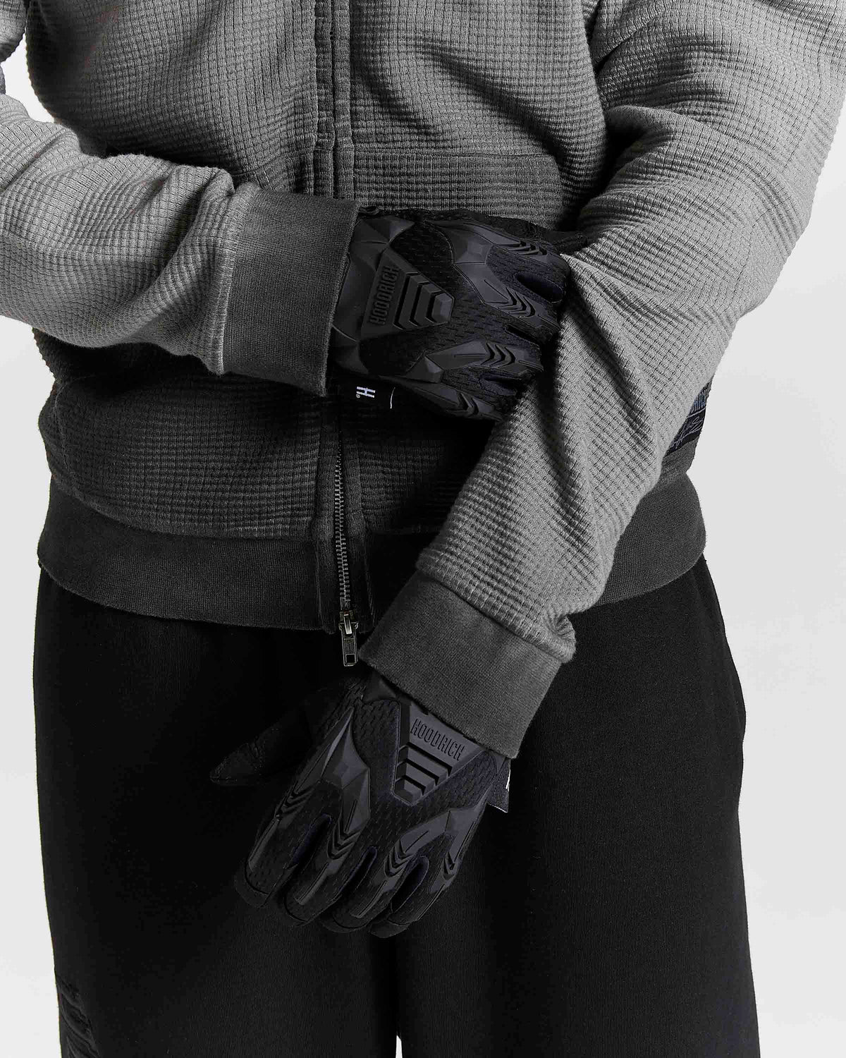 Black winter gloves with textured grip panels and ribbed cuffs, worn by a model in a gray zip-up jacket and black pants.