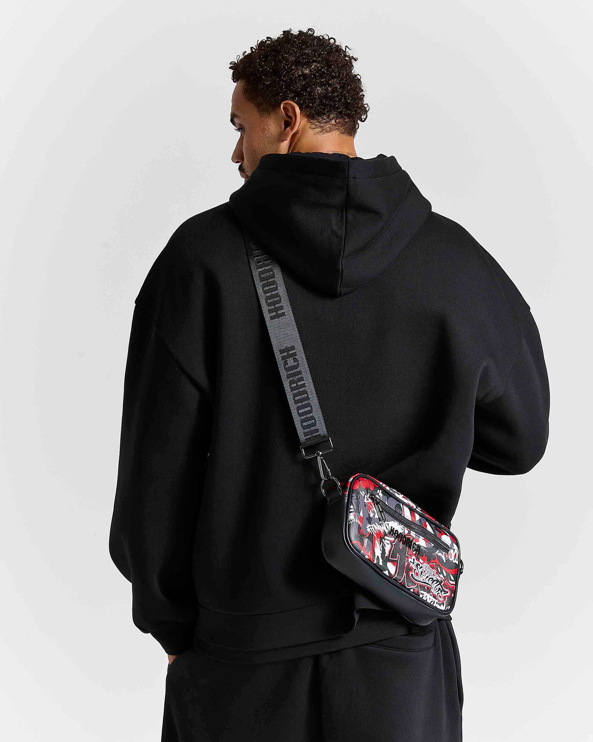 Displays a model wearing the Graffiti 'Hoodrich' branded Crossbody Bag