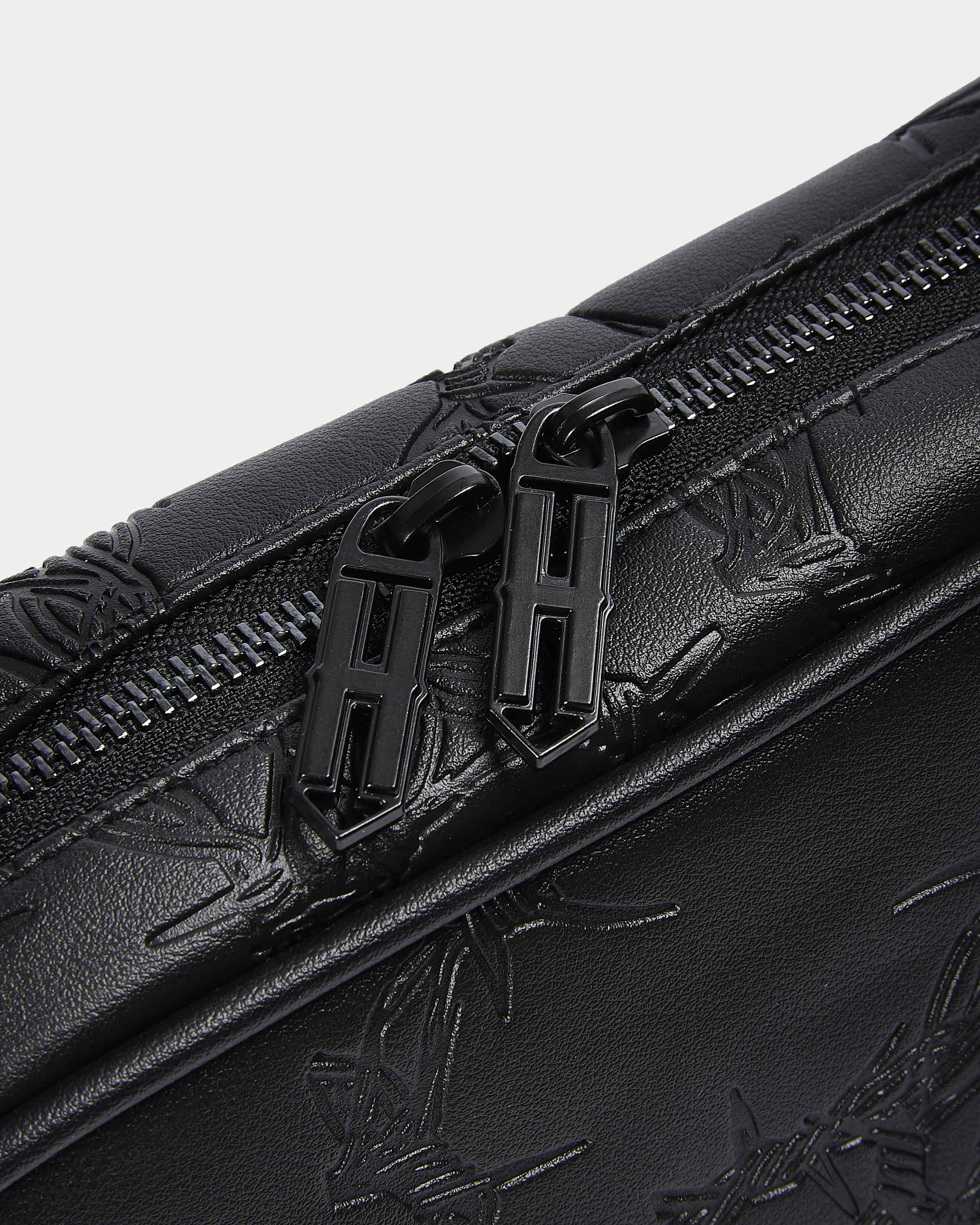 Close-up of a black leather bag with floral embossing and zipper details on a light gray background.