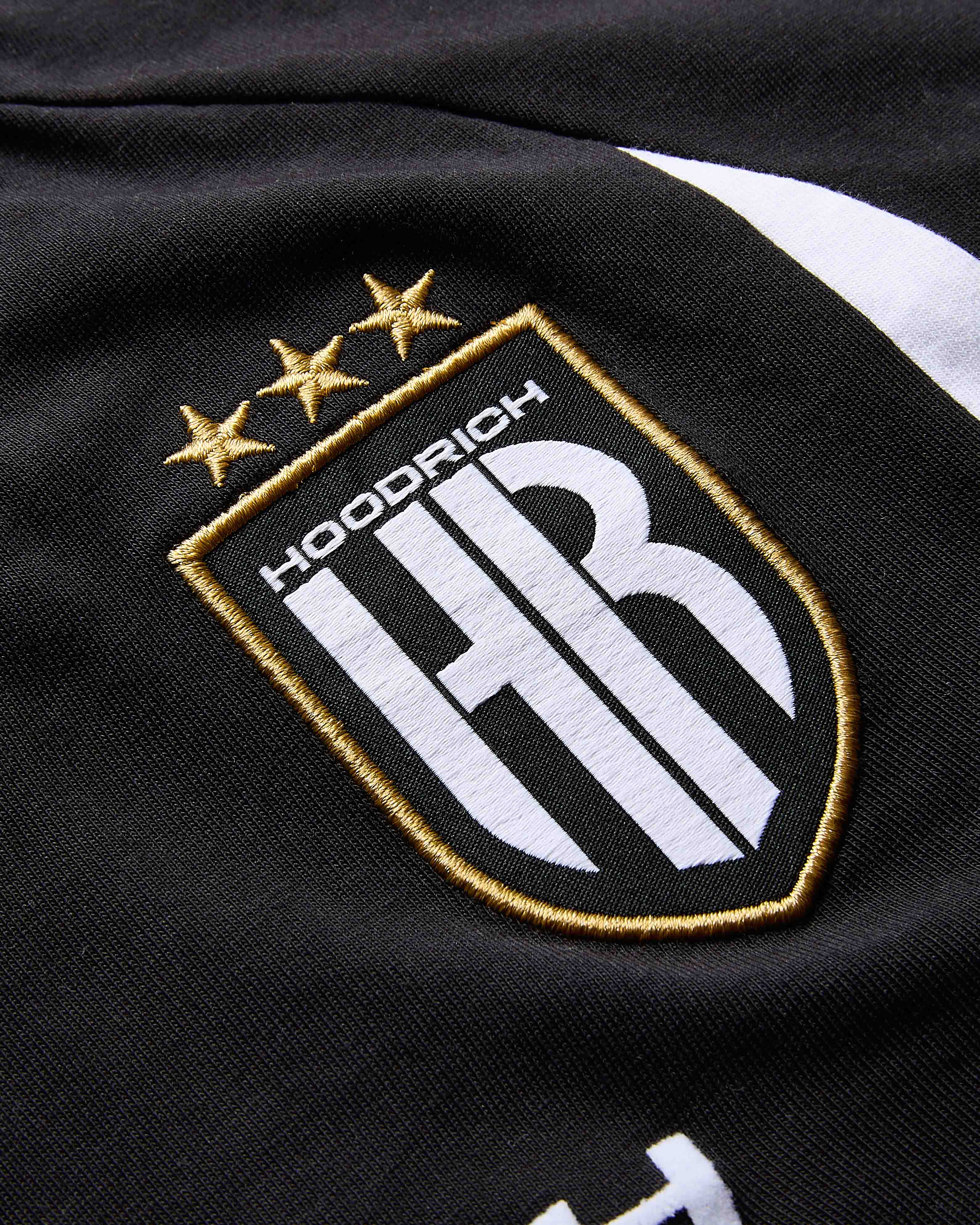 Close-up of a black jacket with an embroidered logo featuring stars and 'Hoodrich' text.