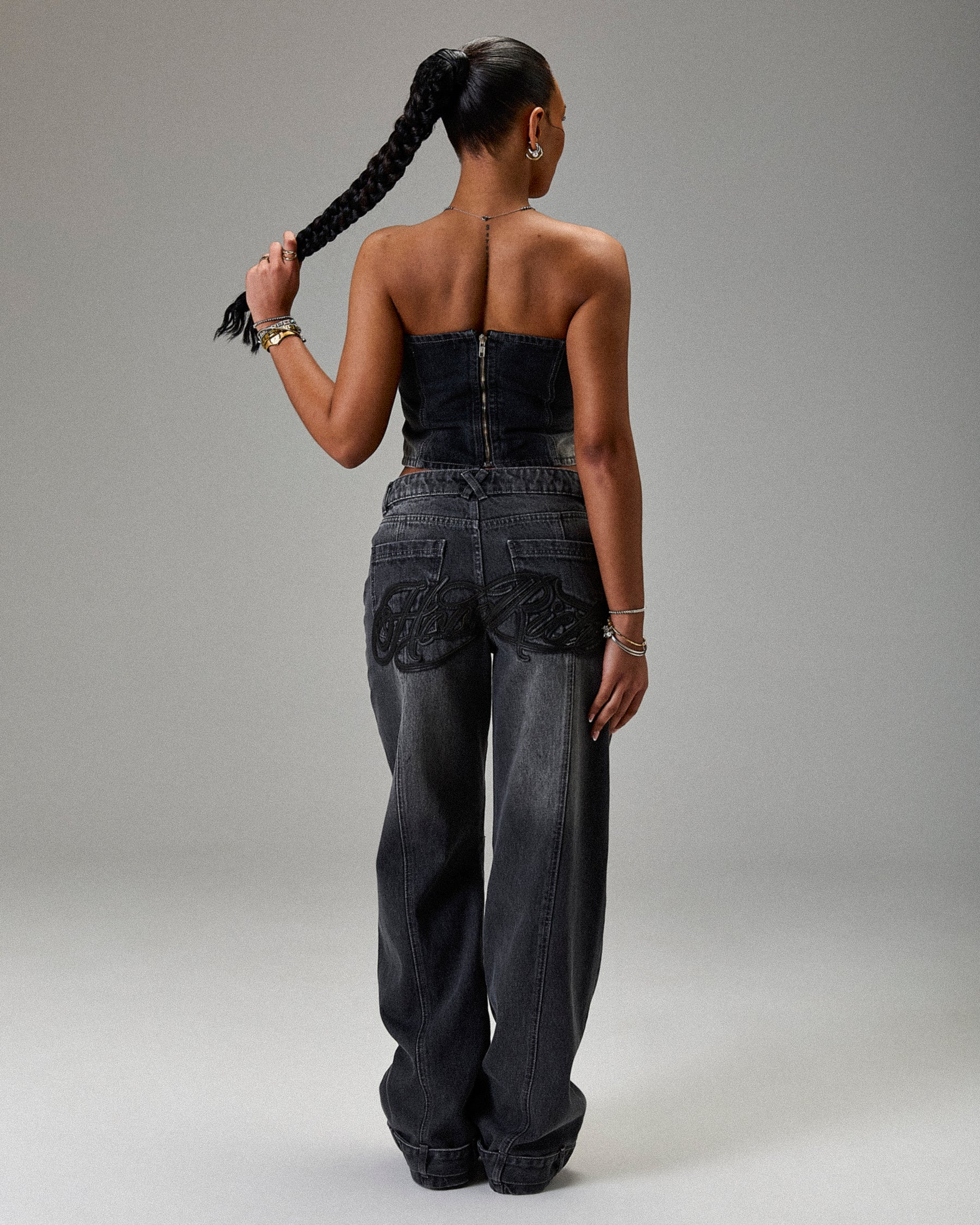 Woman wearing a strapless top and dark jeans with decorative elements on a gray background