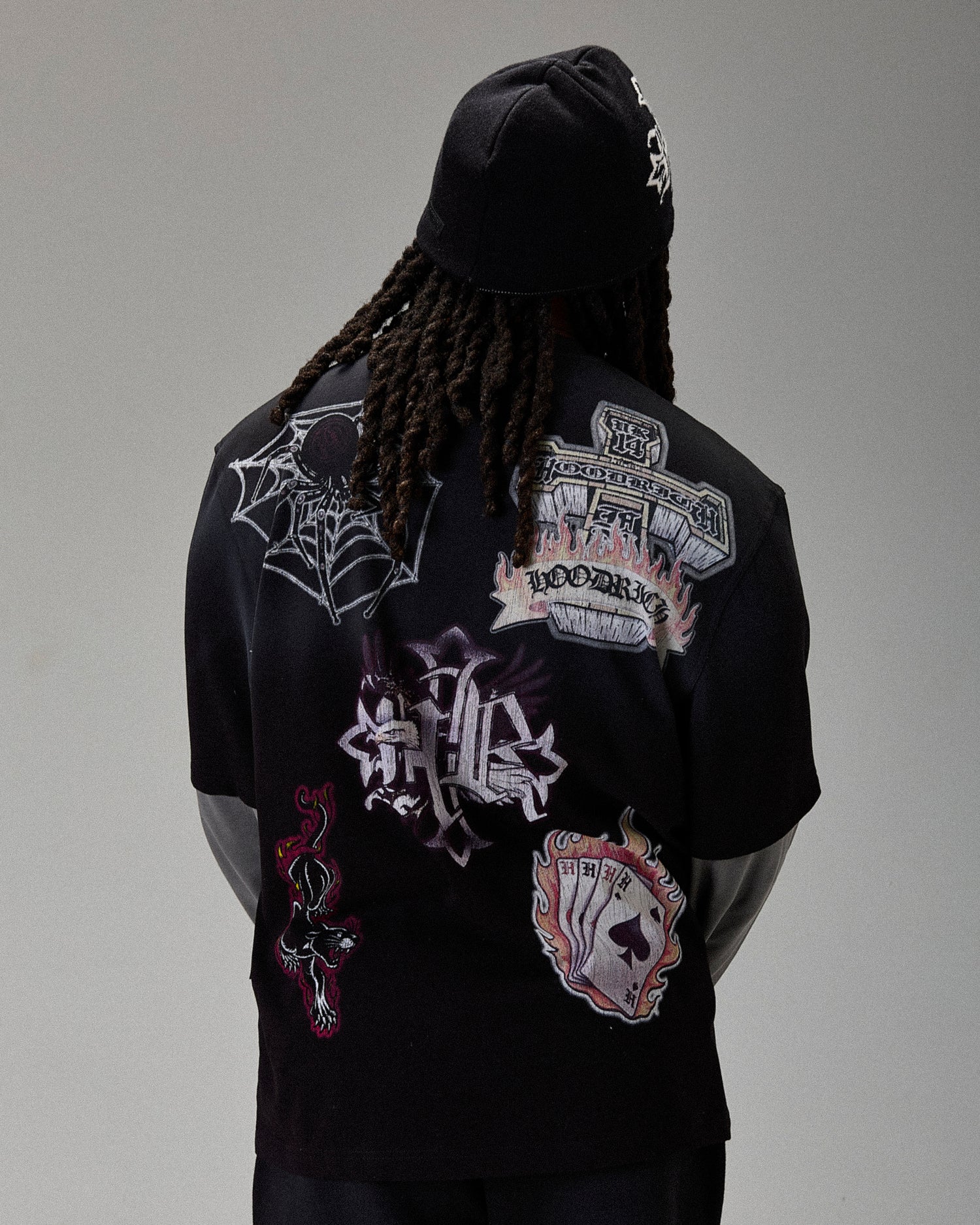 Person wearing a black hoodie with various patches on the back against a gray background