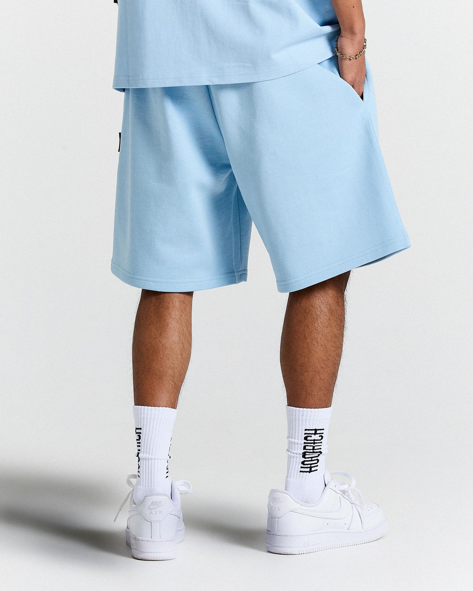 Person wearing light blue shorts and white sneakers on a plain background