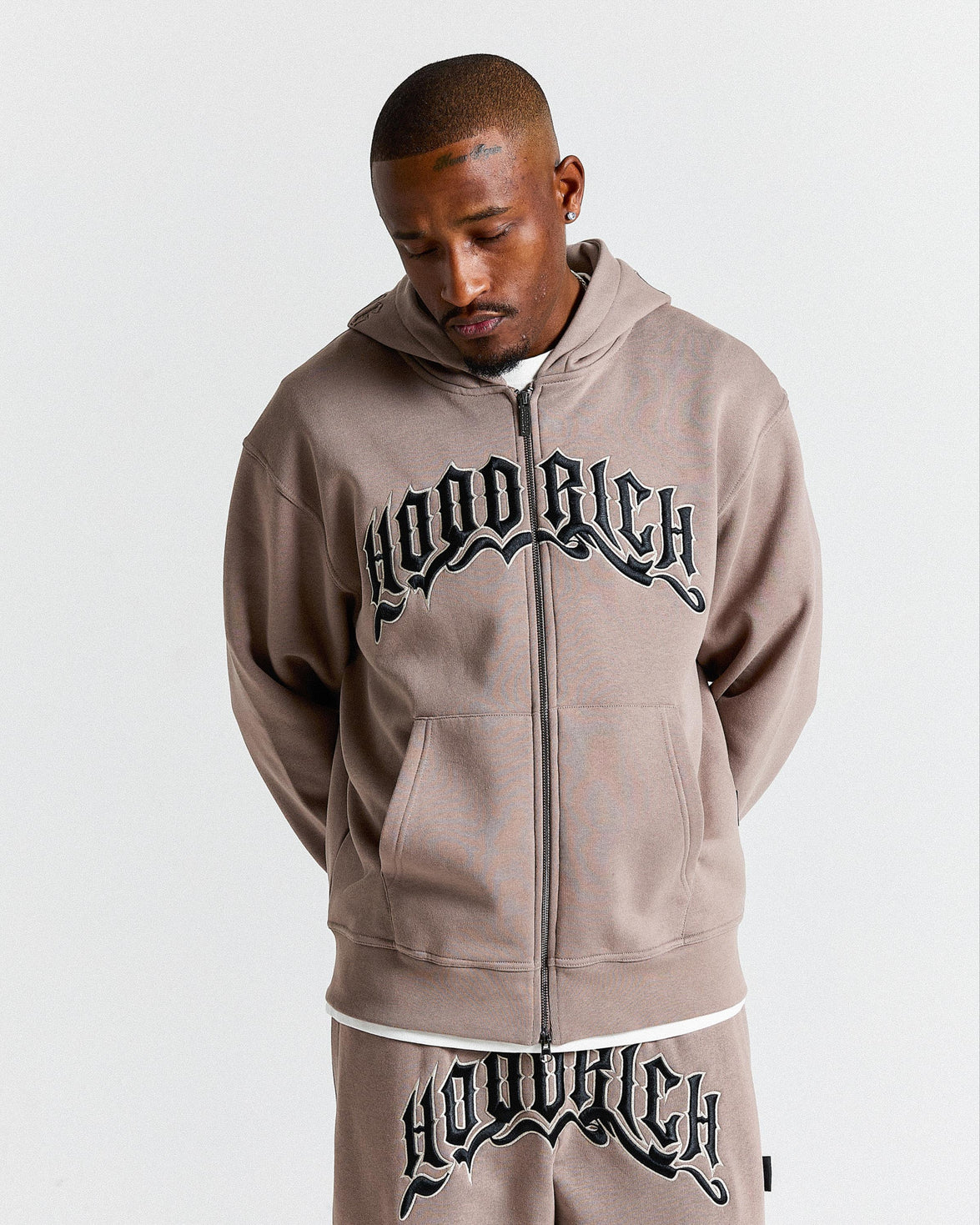 Man wearing a 'Hood Rich' hoodie and pants on a light gray background
