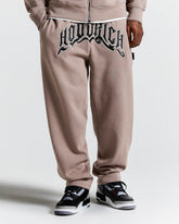 Brown sweatpants with a brand logo on the back, worn by a person, on a white background.