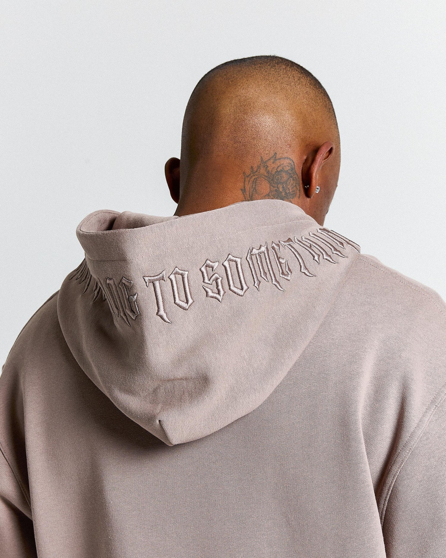 Person wearing a beige hoodie with text on the back against a light gray background