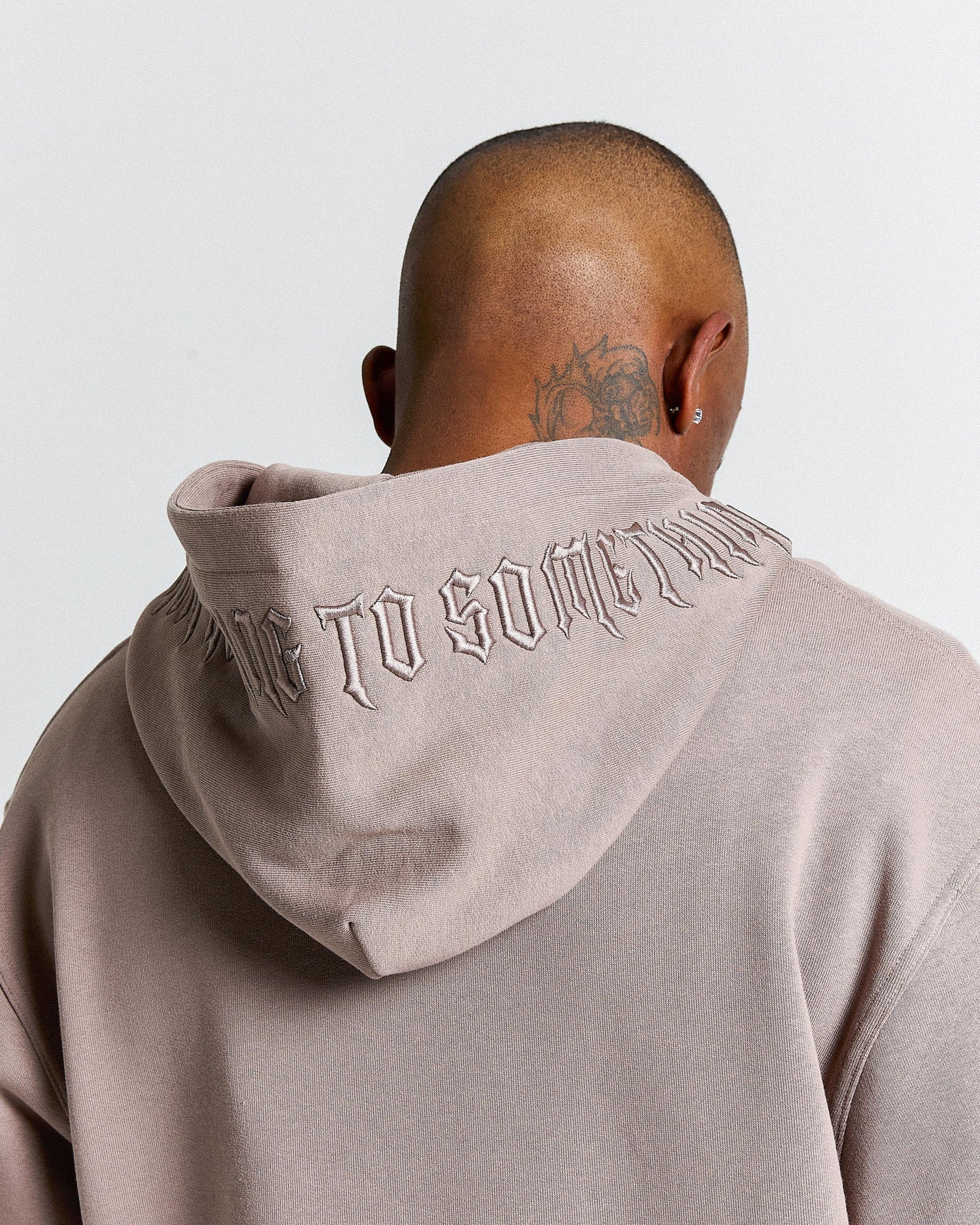 Person wearing a beige hoodie with text on the back against a light gray background