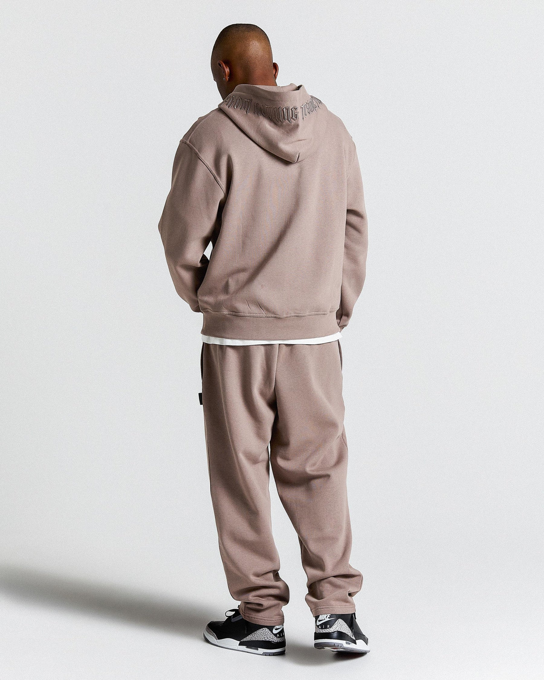 Person wearing a beige tracksuit with a hood on a white background
