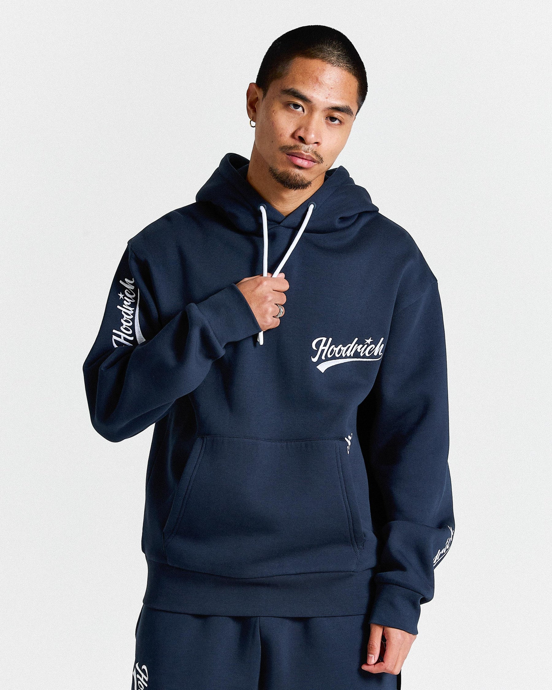 Man wearing a navy blue hoodie with 'Hoodrich' branding on a light gray background