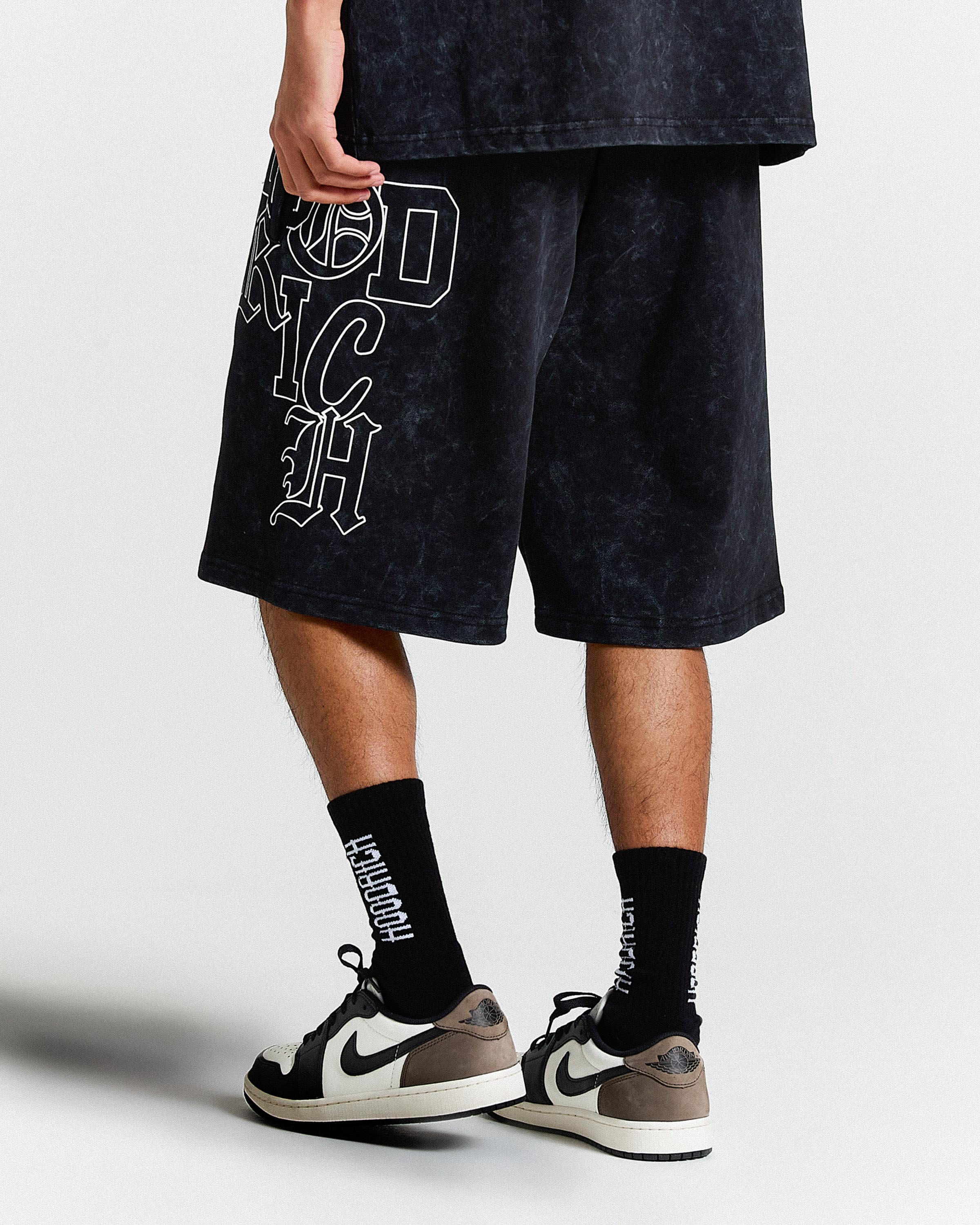 Person wearing black shorts with graphic design and black socks with text, standing against a white background.