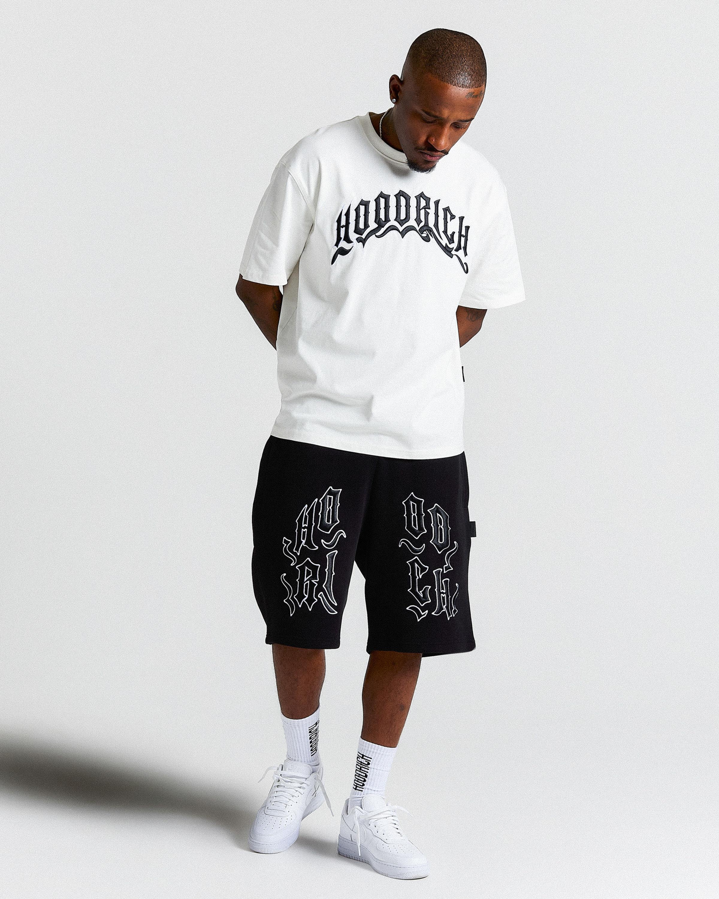 Man wearing white 'HOODRICH' branded T Shirt and black 'HOODRICH' branded shorts.