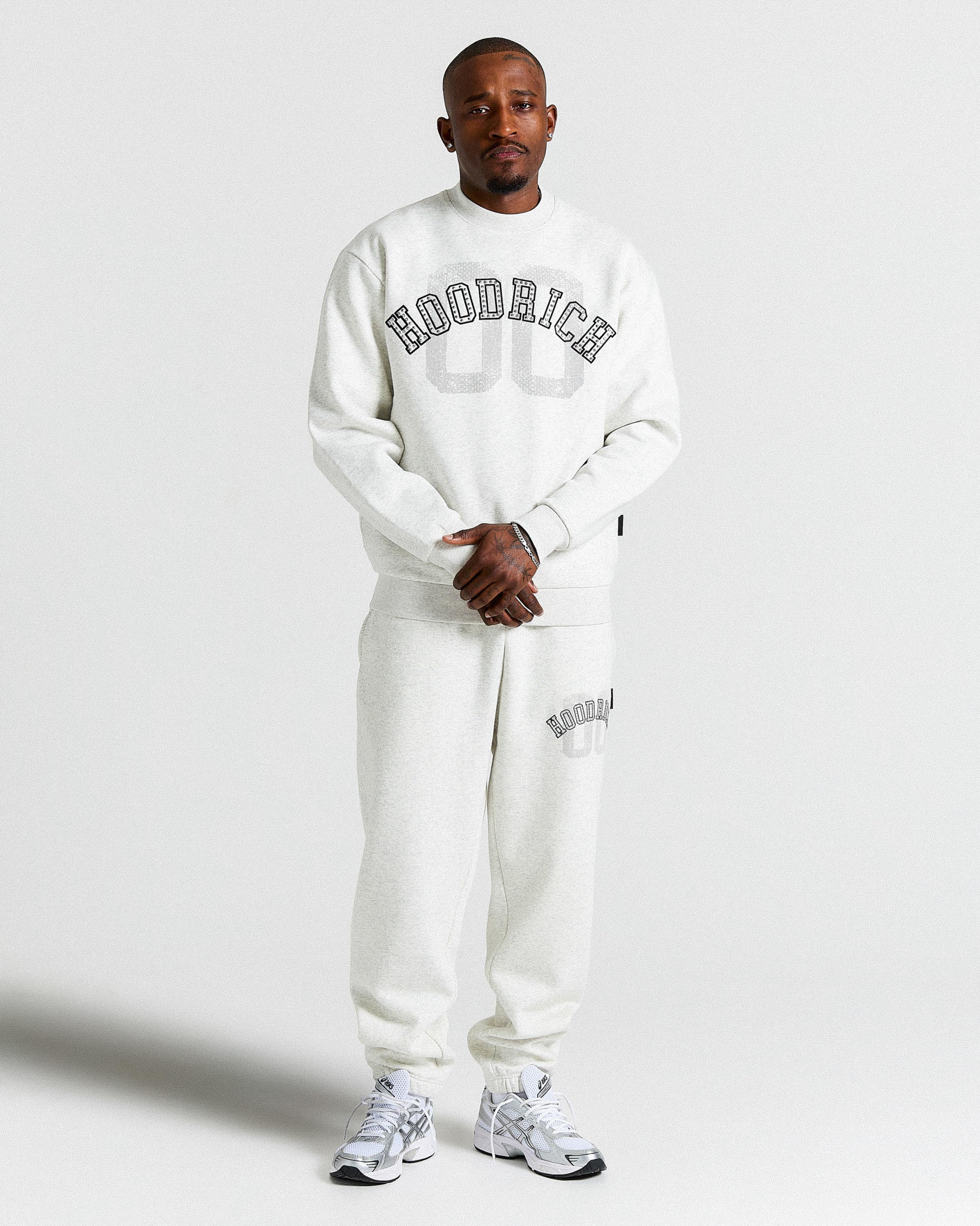 Person wearing a light grey 'Hoodrich' sweatshirt and pants on a plain background