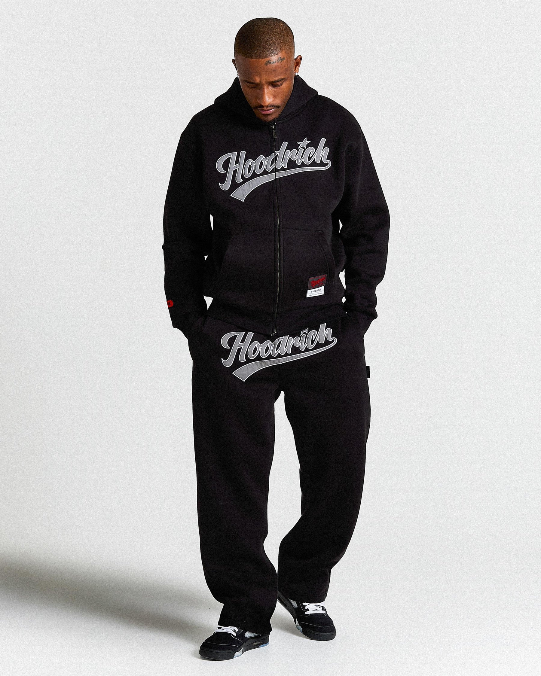 Person wearing a black hoodie and pants with 'Hoodrich' branding on a white background