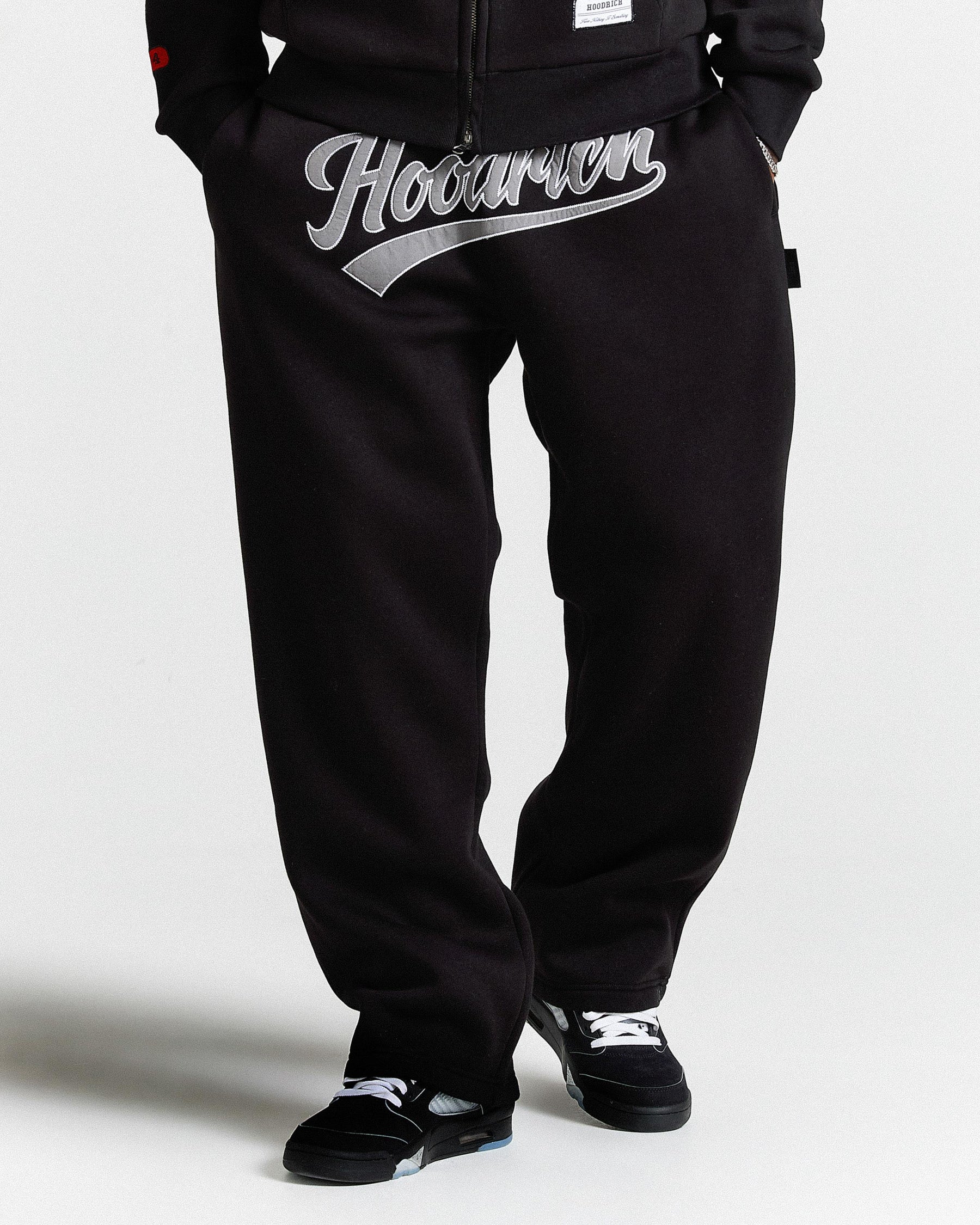 Black pants with 'Hoodrich' logo worn by a person on a white background