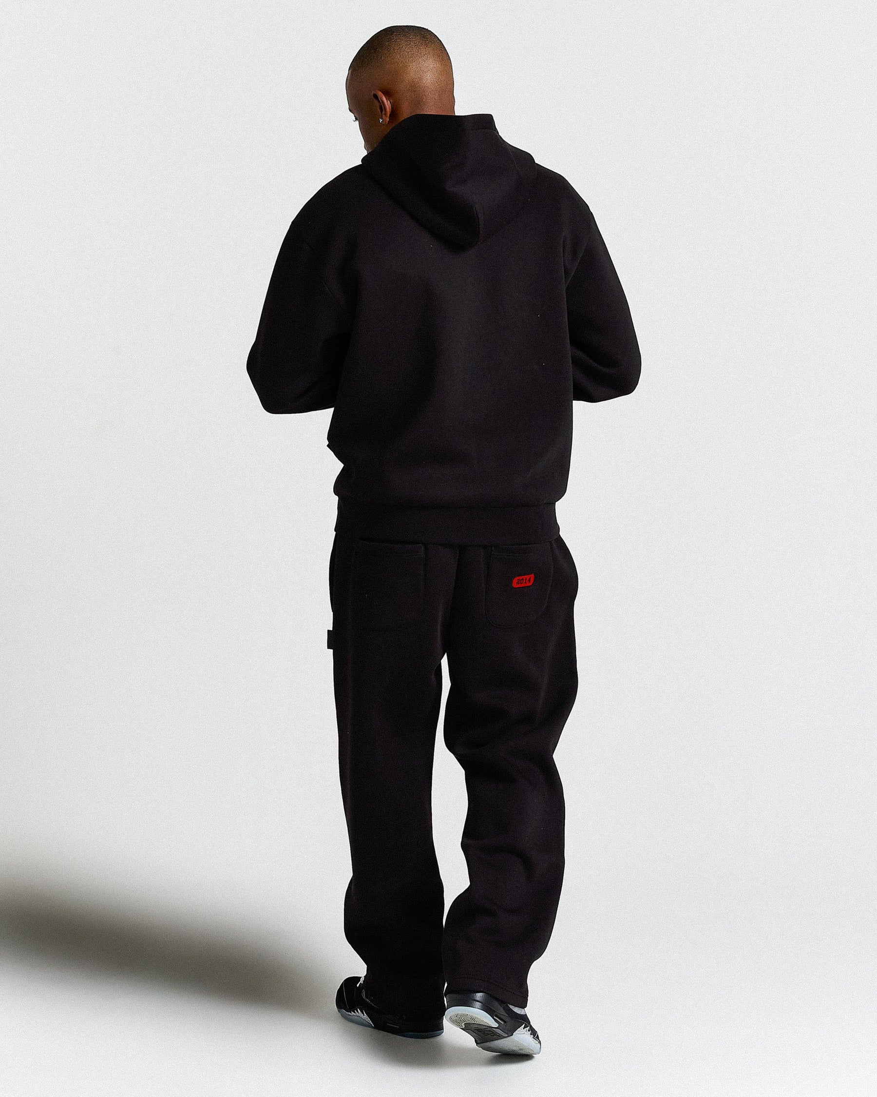 Person wearing a black tracksuit with a red logo on a white background