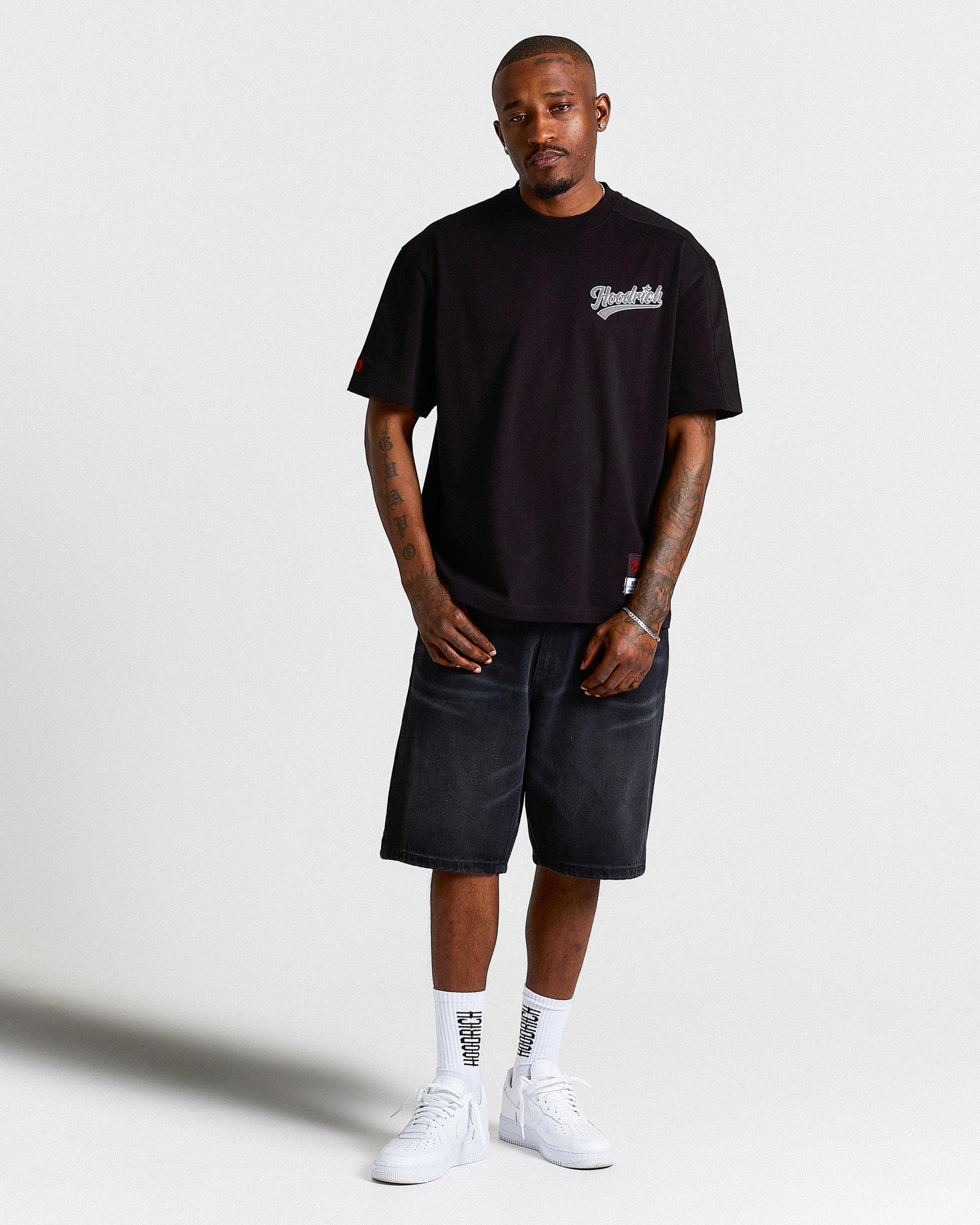 Man wearing a black t-shirt and denim shorts on a white background