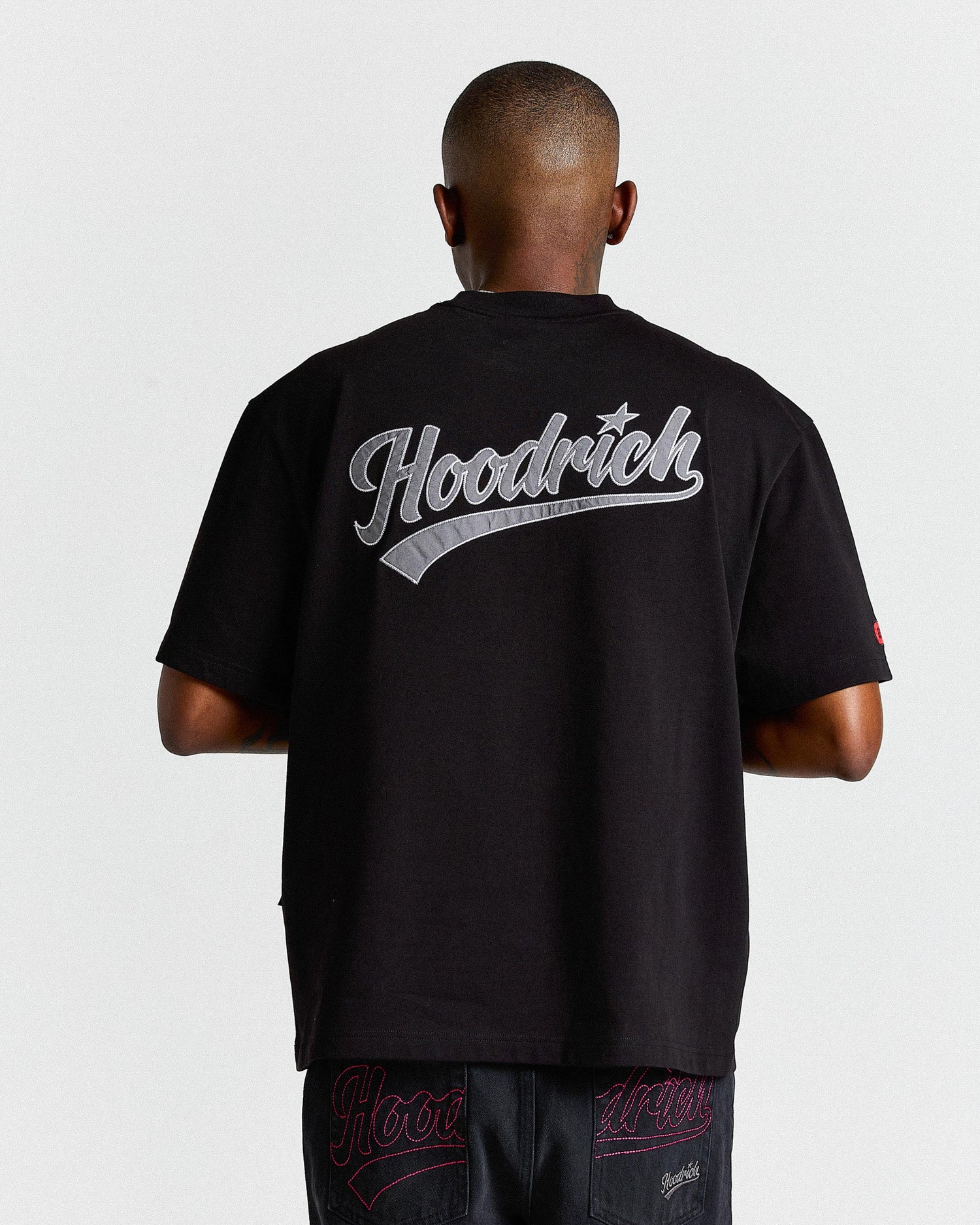 Person wearing a black 'Hoodrich' t-shirt with branding on the back against a white background