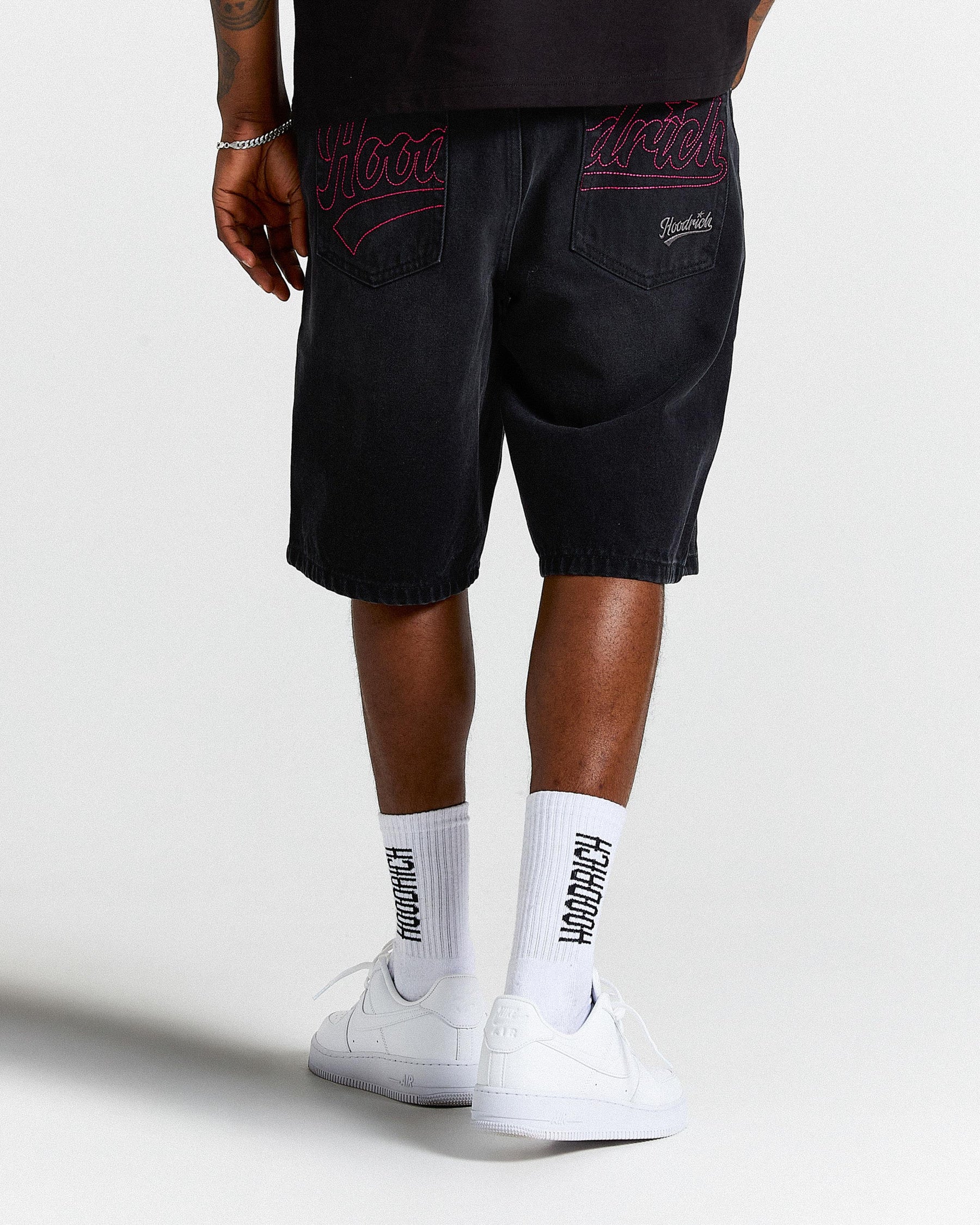 Person wearing black shorts with red embroidery and white socks with text, standing against a white background