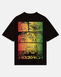 A black short-sleeve graphic t-shirt featuring a large rectangular multicolor print on the front. The graphic is divided into four panels with a red, yellow, and green gradient, showing a collage of faces and text at the bottom reading 'POST CARNIVAL CLASH MASH PORTOBELLO ROAD LONDON SUNDAY 10-4:30' and 'HOODRICH'.