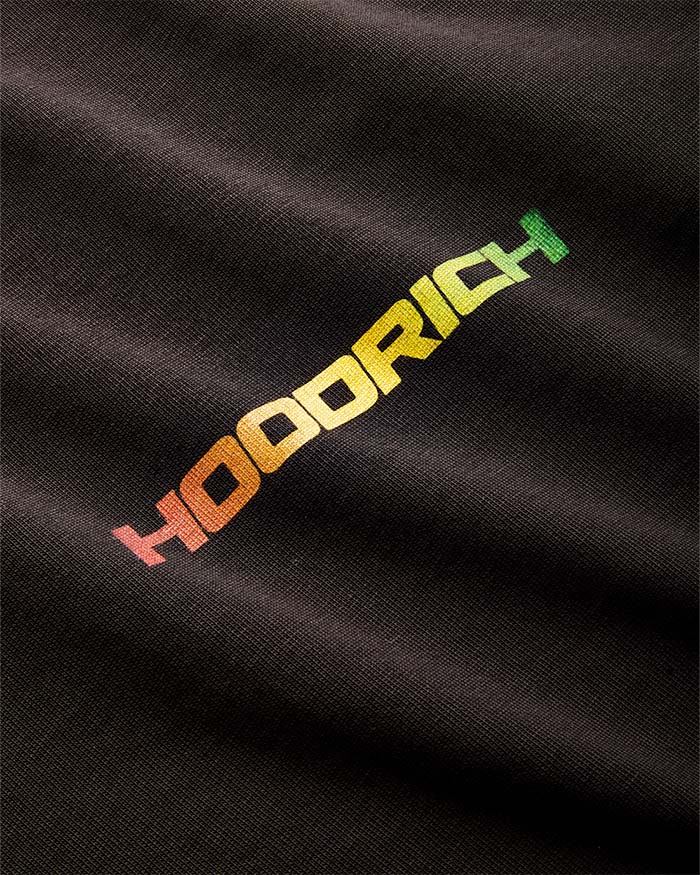 Close-up of a black textured fabric with a diagonal embroidered 'HOODRICH' logo in a red, orange, yellow, and green gradient.