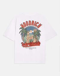 A white short-sleeve t-shirt shown from the back, featuring a large graphic print with the brand name 'HOODRICH' in red arched letters above a retro illustration of a building and palm trees, and 'Worldwide' in red script below.