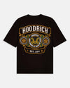 A black short-sleeve t-shirt with a large graphic print on the front. The graphic features the brand name 'HOODRICH' in white letters inside a gold-bordered arch, with circular medallions containing gold stars and a central gold double-horns emblem, and 'EST 2014.