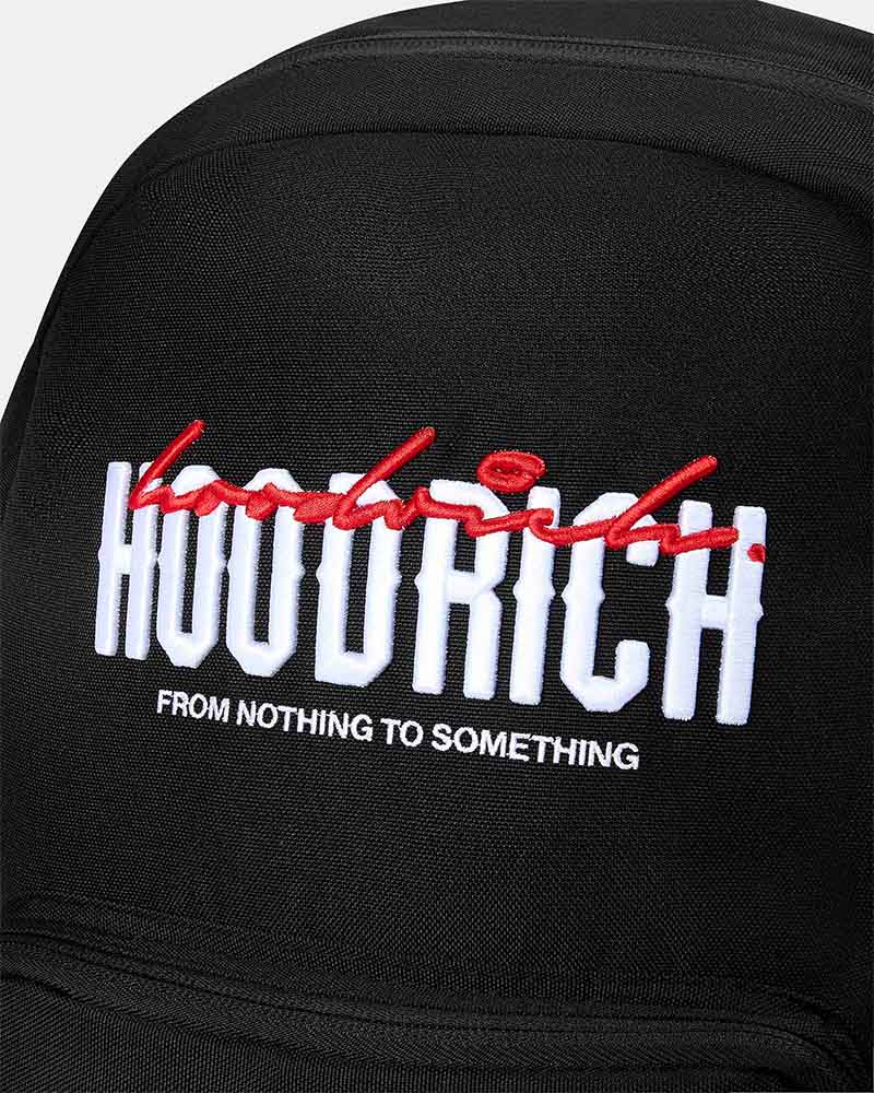 Close-up of a black fabric cap featuring a large white embroidered 'HOODRICH' logo with a red script overlay and the phrase 'FROM NOTHING TO SOMETHING' in white below.
