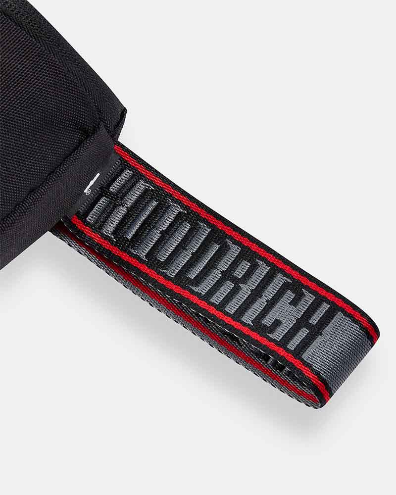 Close-up of a black fabric strap with a wide woven label reading 'HOODRICH' in gray, bordered by red stitching