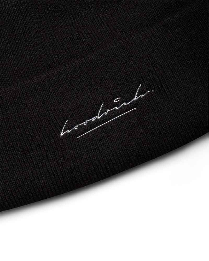 Close-up of a black ribbed knit fabric with a small white embroidered script logo reading 'Hoodrich.'
