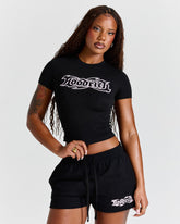 Woman wearing a black 'Hoodrich' t-shirt and shorts on a white background