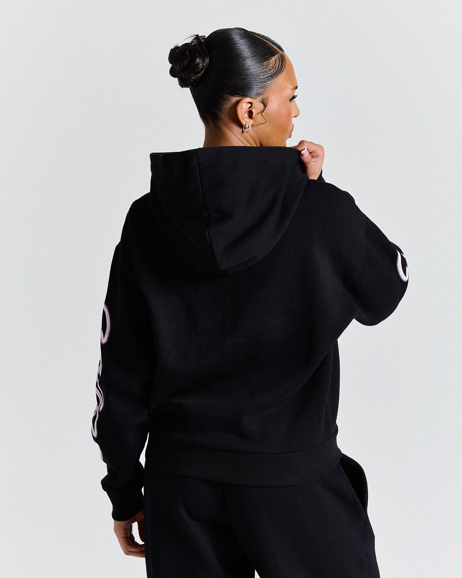 Person wearing a black hoodie with a logo on the sleeve against a light gray background