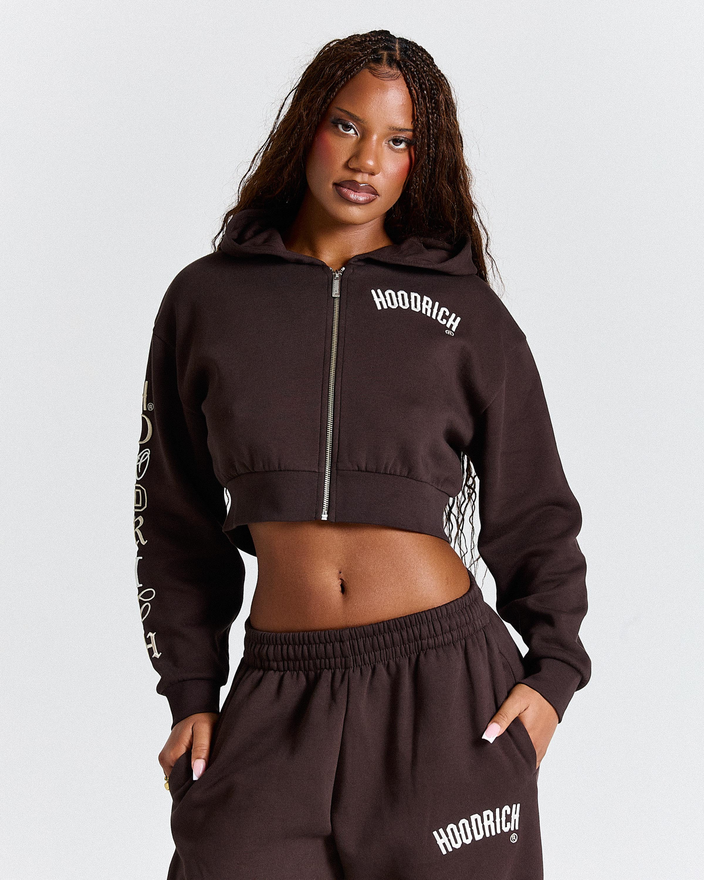 Woman wearing a brown 'Hoodrich' hoodie and pants on a white background