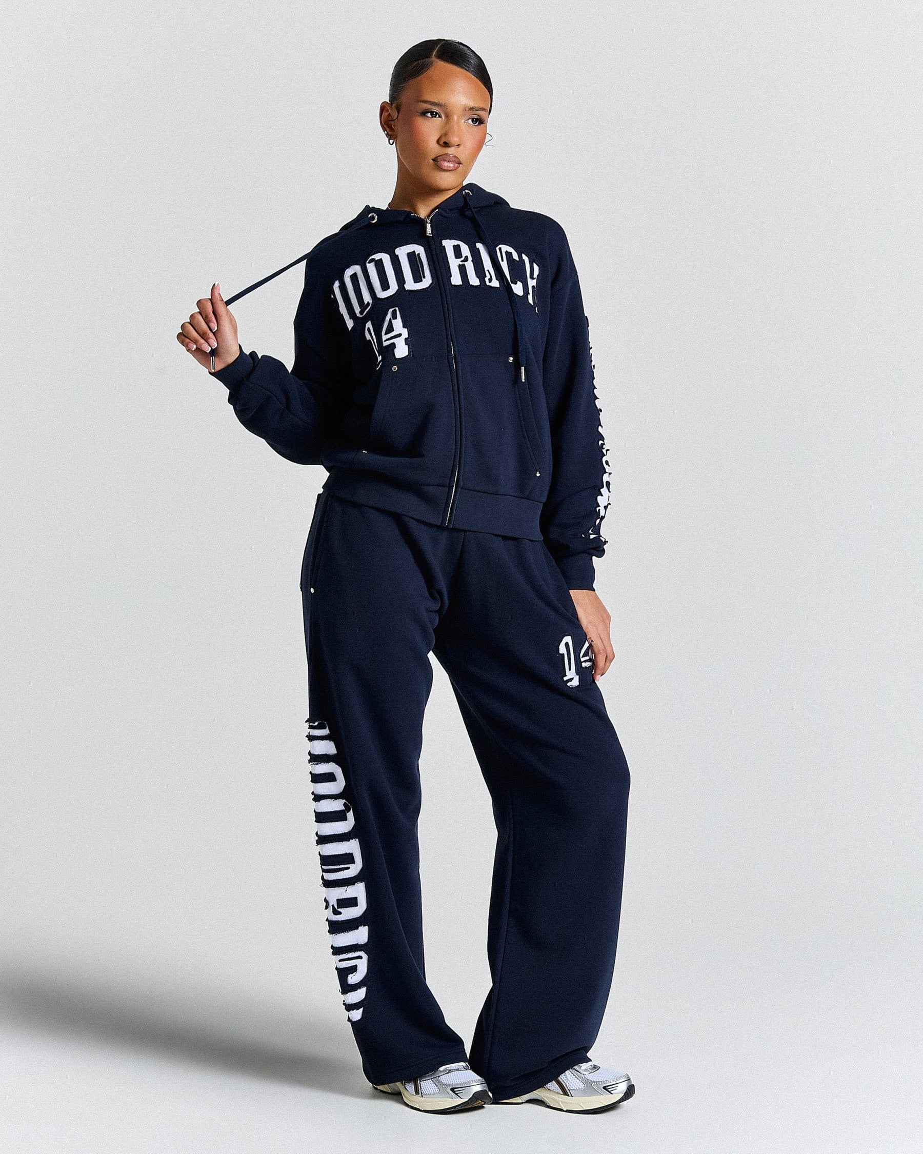 Person wearing a navy tracksuit with 'HOODRICH' branding on a light gray background