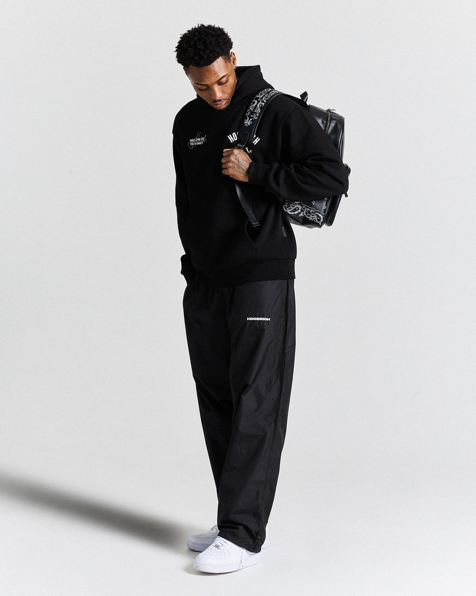 Man wearing a black tracksuit with a graphic backpack on a light gray background