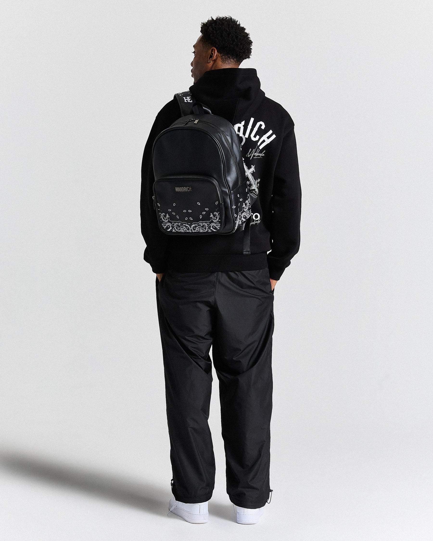 Person wearing a black hoodie with a brand logo and a black backpack on a white background