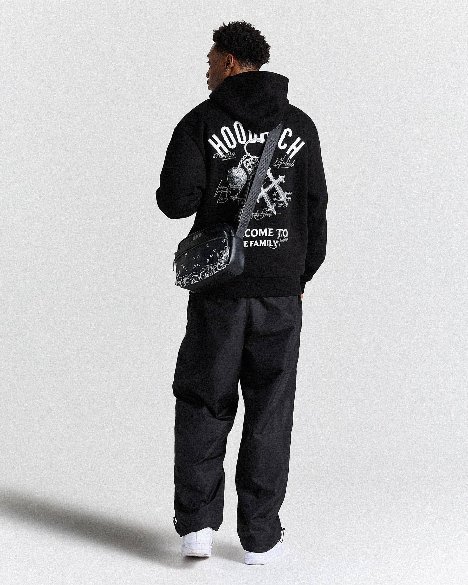 Person wearing a black hoodie with text and graphics on the back, standing against a white background.