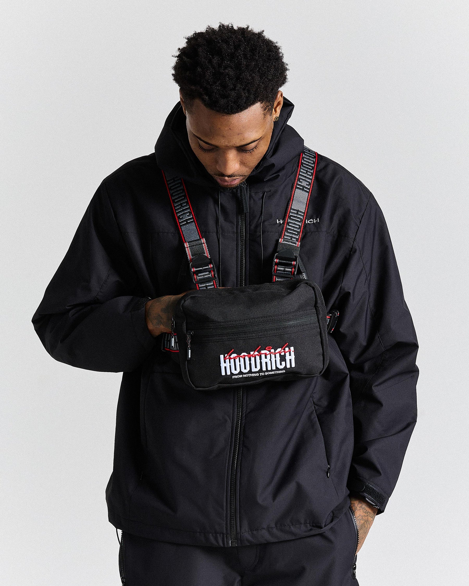 Person wearing a black jacket and a black bag with 'HOODRICH' branding on a white background.