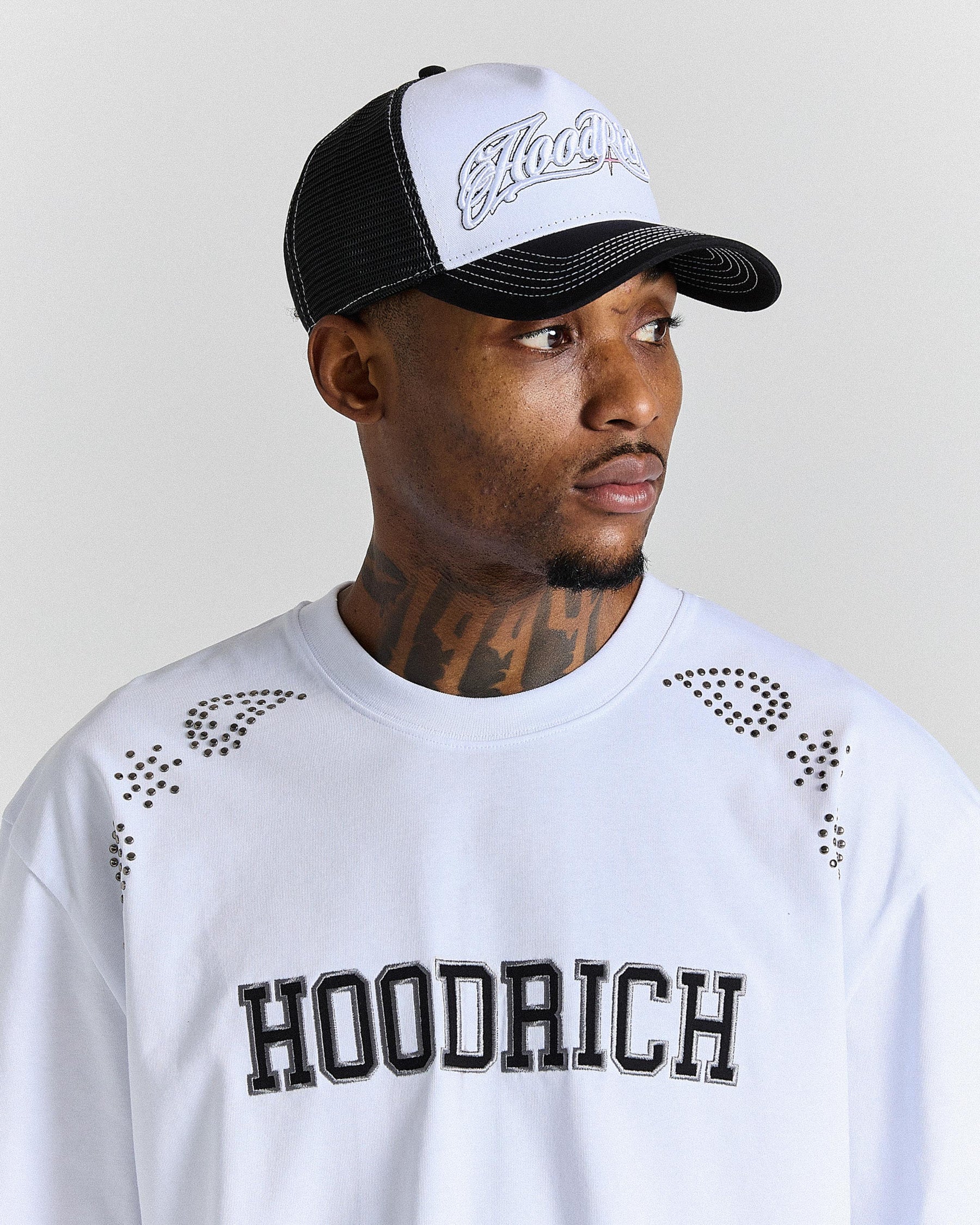 Man wearing a black and white cap and a white sweatshirt with 'Hoodrich' text.