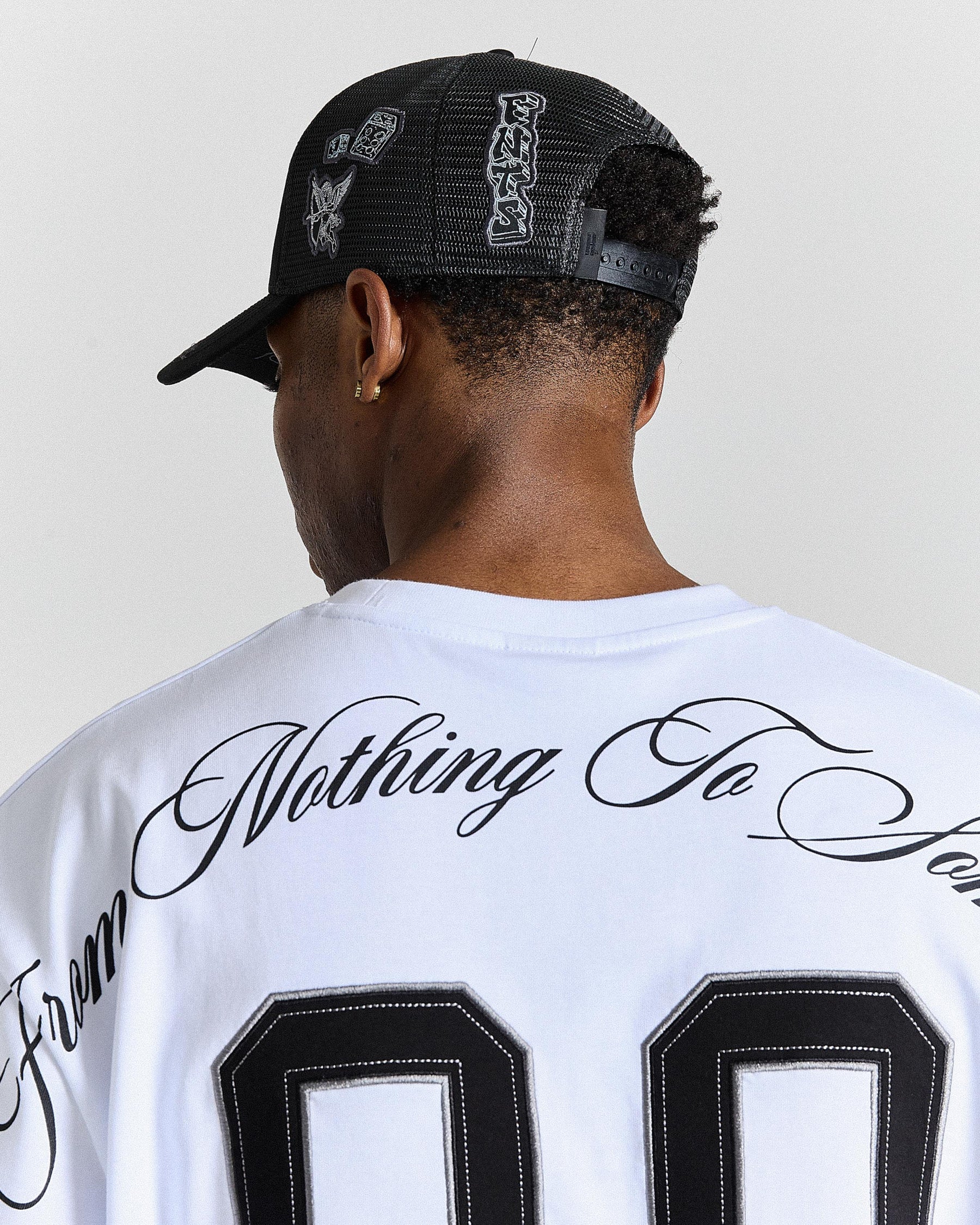 Person wearing a white jersey with text and a black cap on a plain background