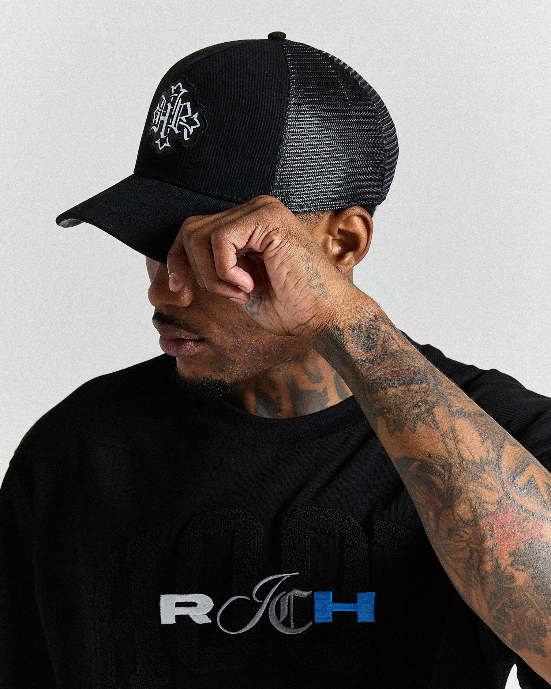 Man wearing a black cap and black shirt with visible branding, against a plain background