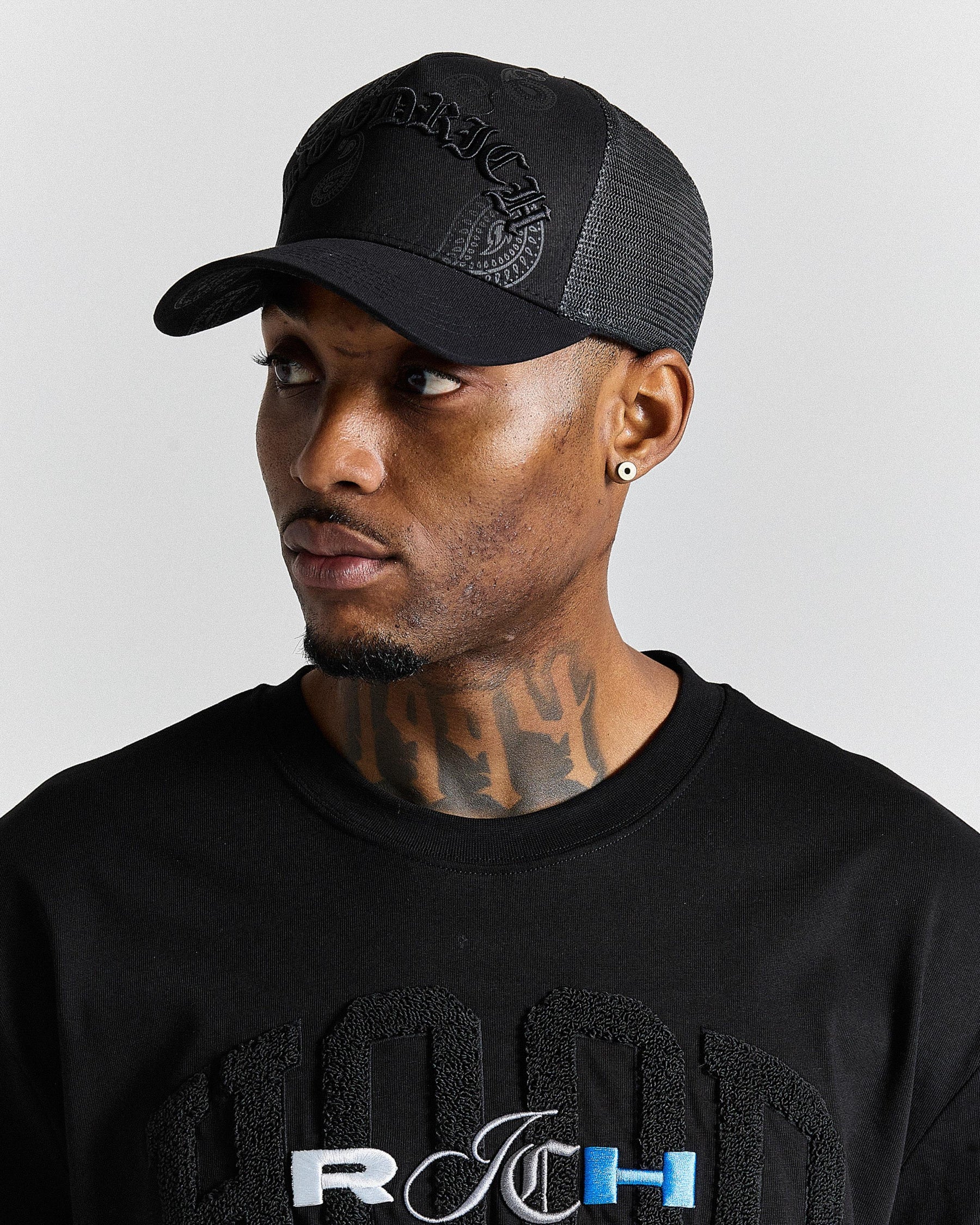 Man wearing a black cap and black shirt with visible branding on a gray background