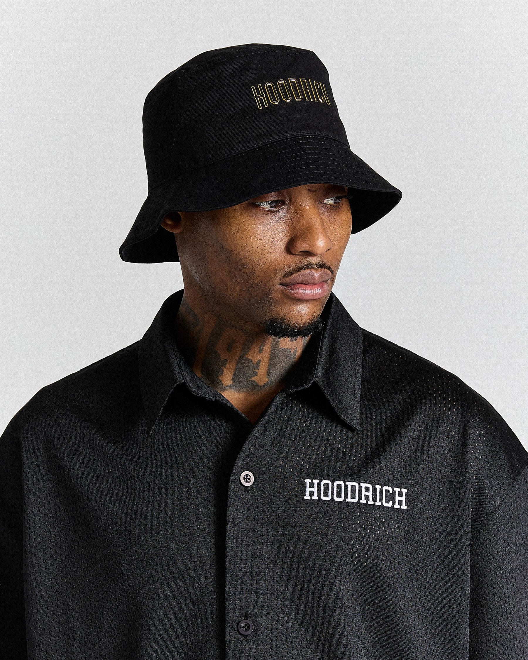 Man wearing a black bucket hat and black shirt with 'Hoodrich' branding on a gray background