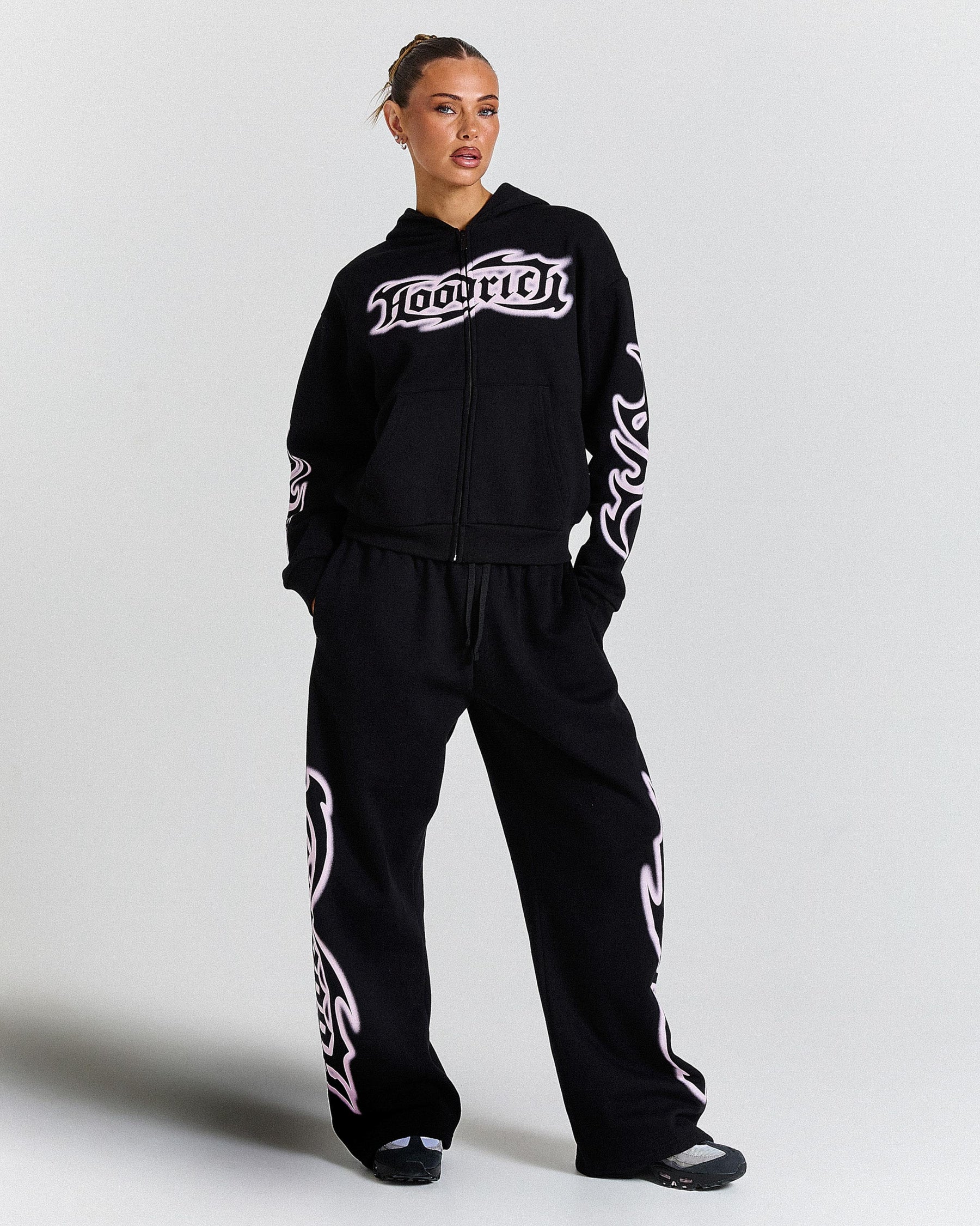 Person wearing a black hoodie and pants with white branding on a light gray background