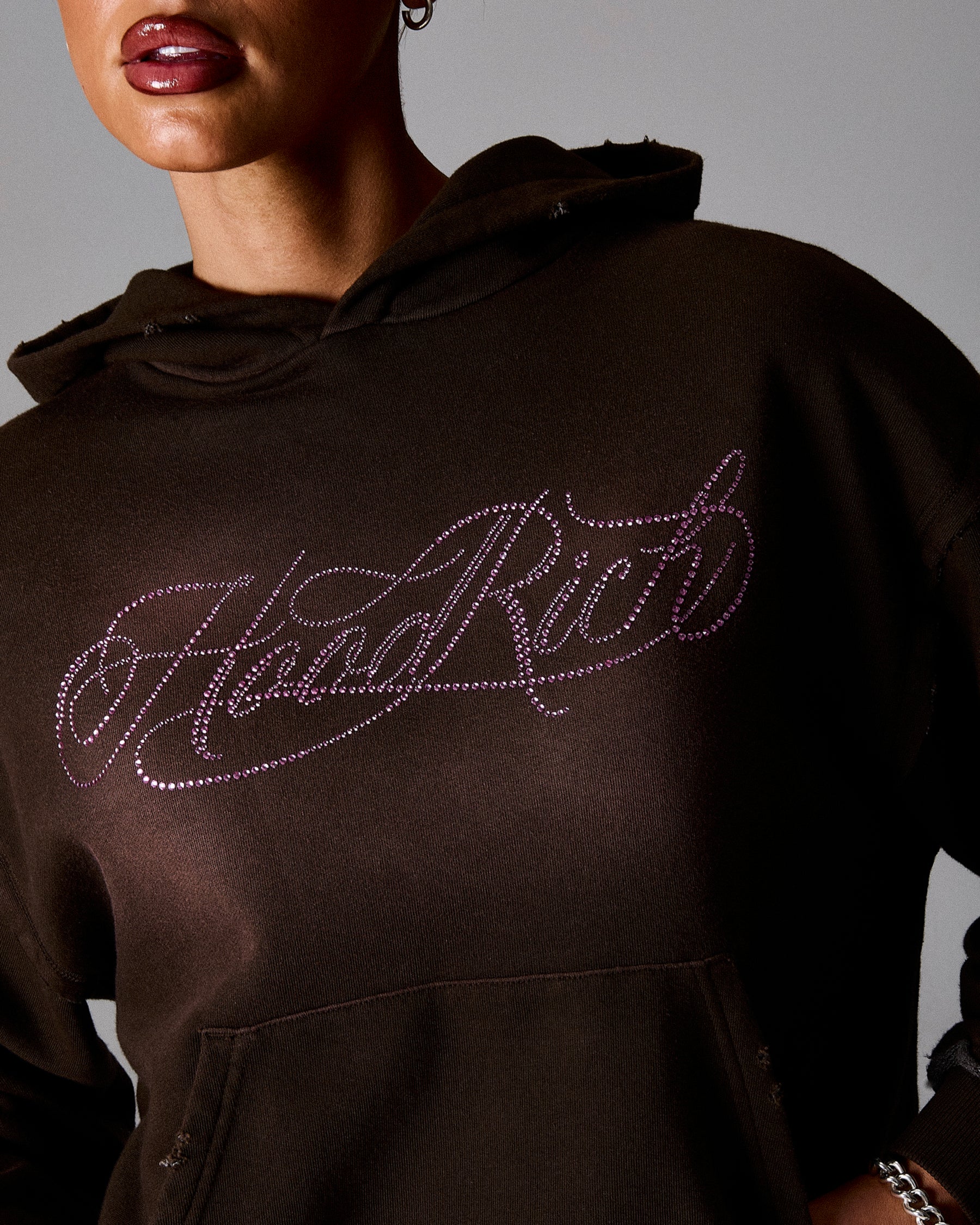 Brown hoodie with 'Hard Rich' text in pink rhinestones on a neutral background