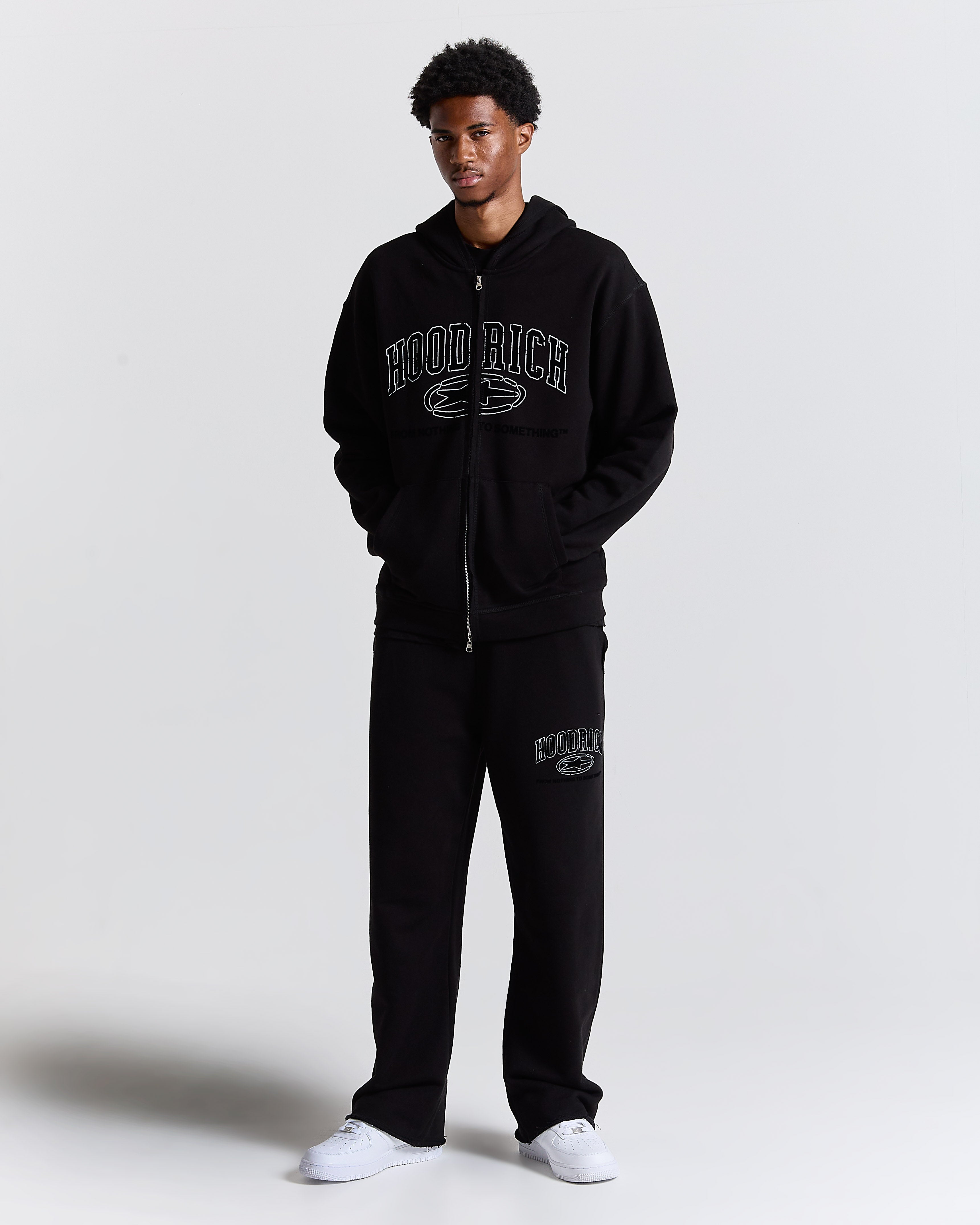 Person wearing a black 'HOODRICH' tracksuit on a white background